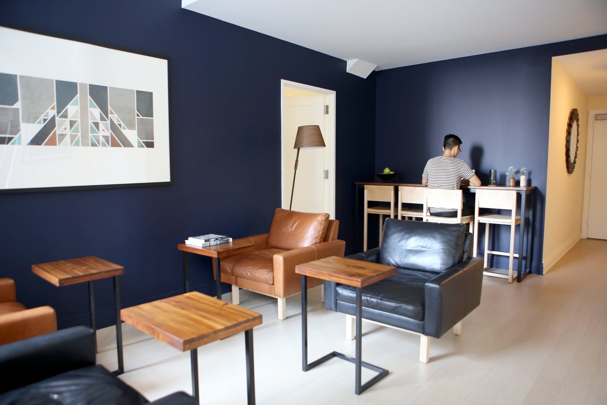 TV lounge at 70 Pine with navy walls, tan and black leather armchairs, walnut side tables and a resident working at the counter