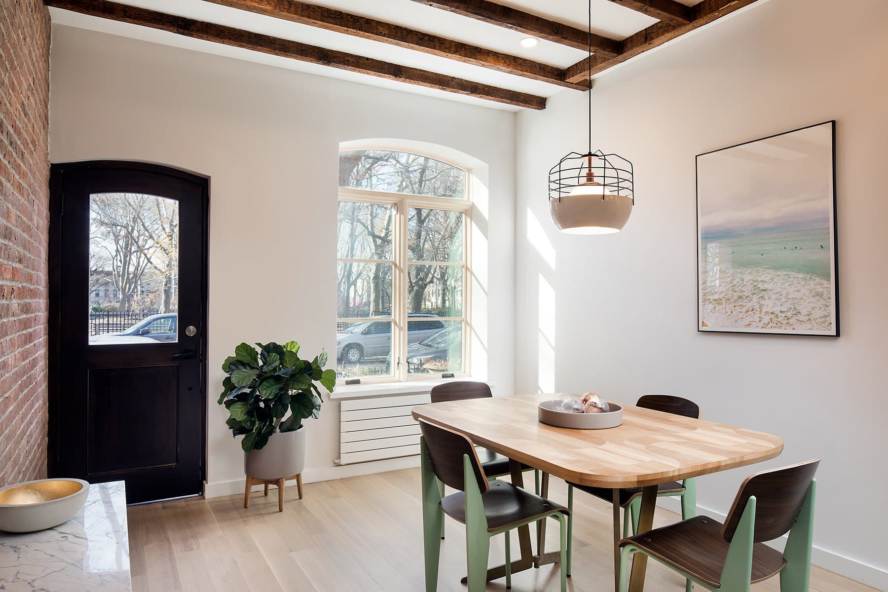 Dining table by the arched front door with green chairs and a pendant lamp in the Greenpoint townhouse