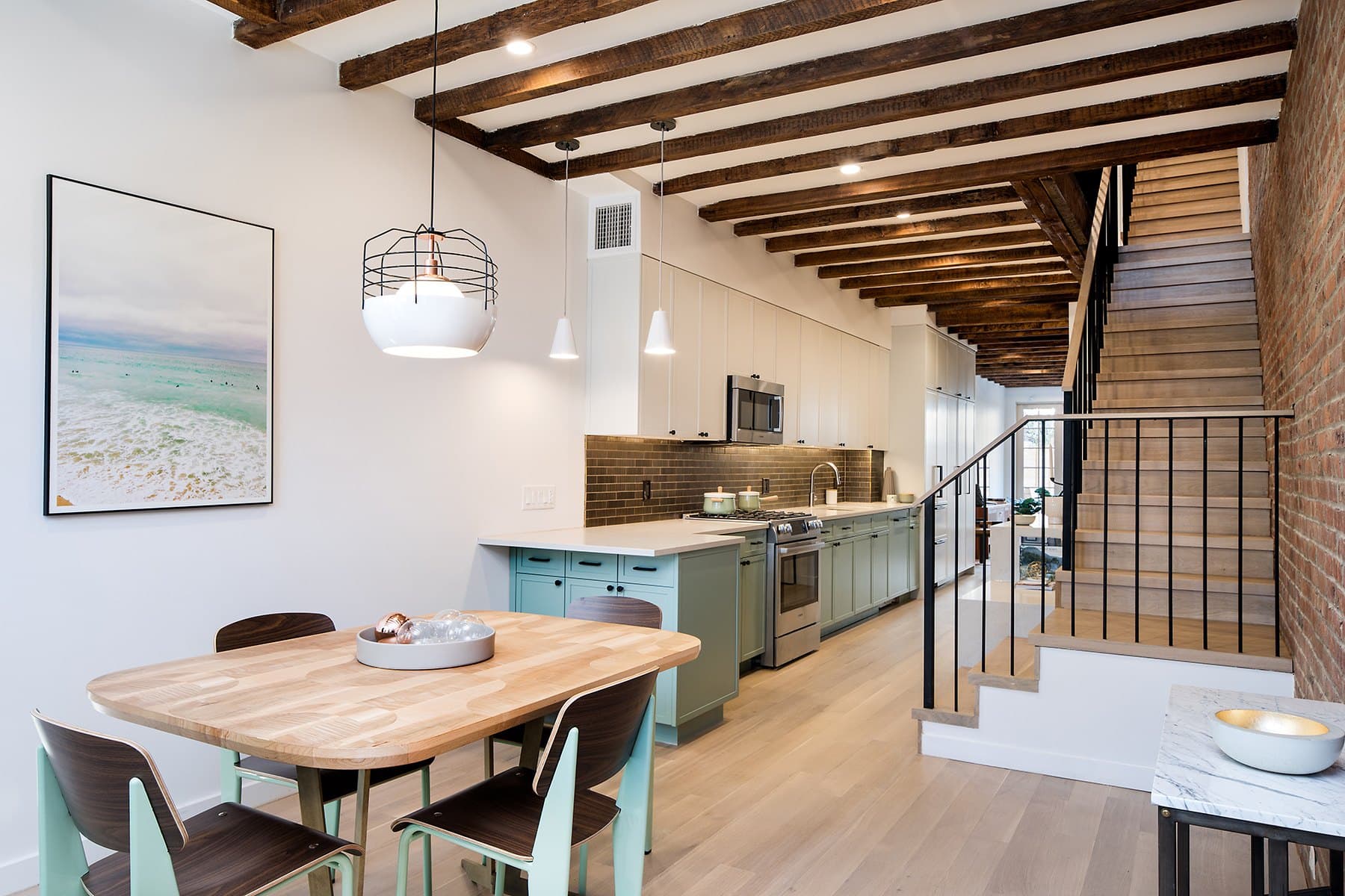 Dining room and sage kitchen of the Greenpoint townhouse at 172 Monitor Street, beneath exposed timber beams with a steel stair beyond