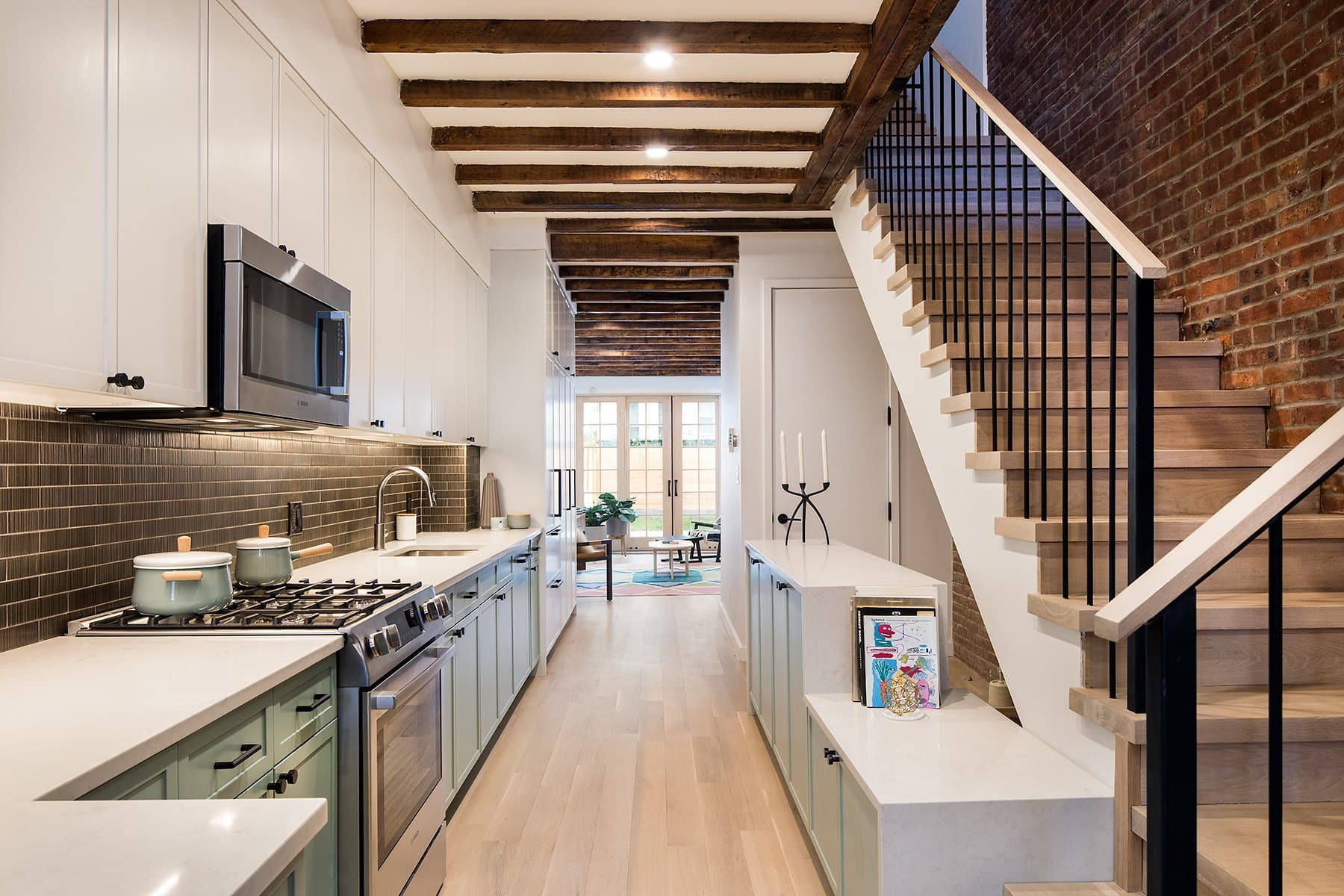 Galley kitchen with sage cabinetry, brown subway tile and a stair along the brick wall