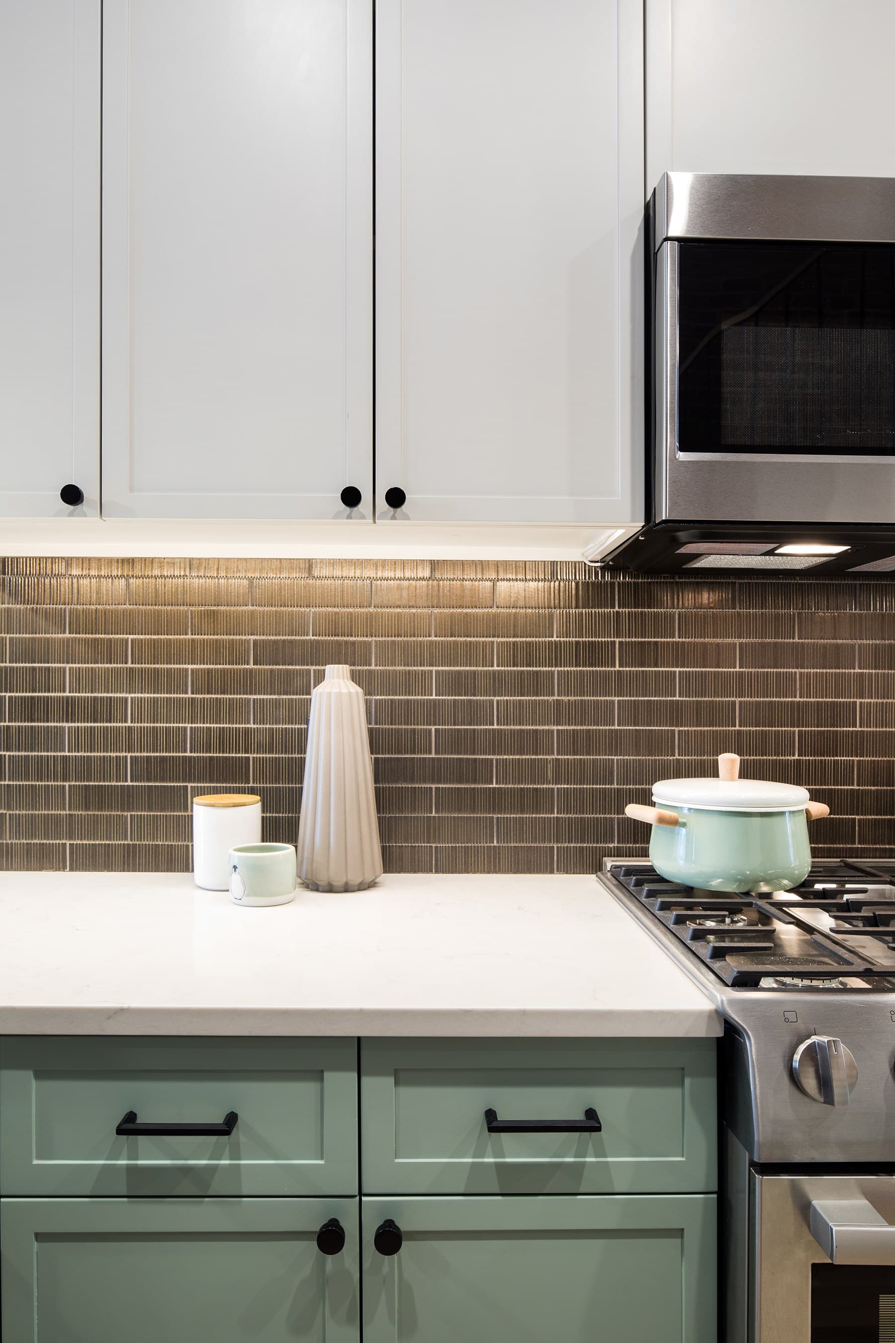 Sage cabinets, brown tile and a white enamel pot on the range