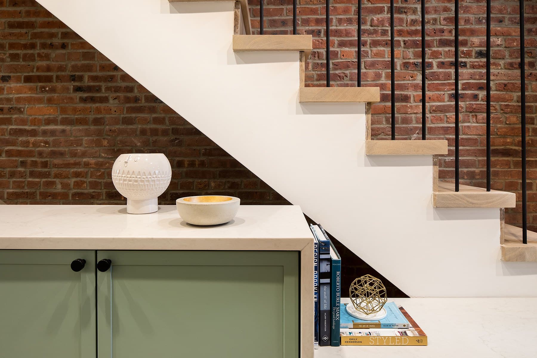 Stair detail with a ceramic vessel on a white counter against brick