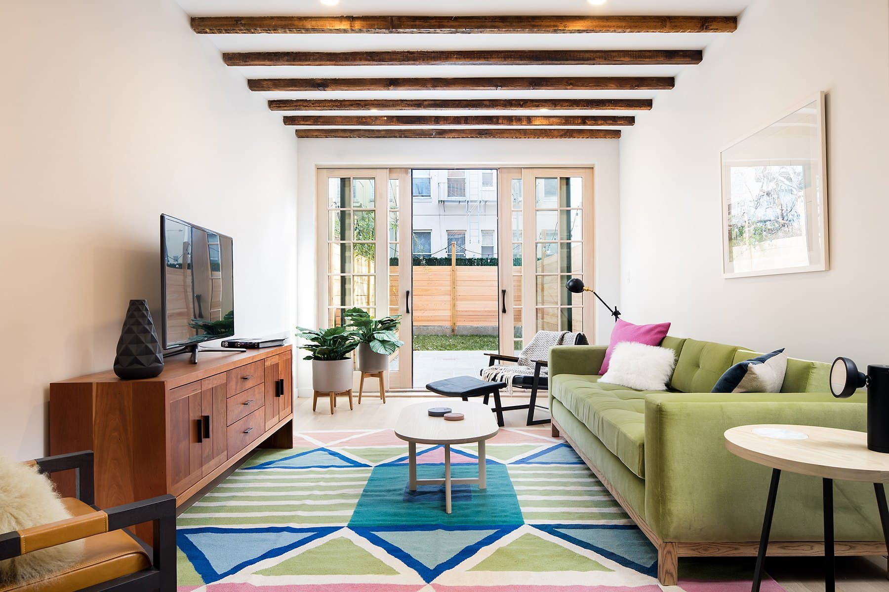 Parlor with a green sofa, a geometric rug, a walnut credenza and exposed timber beams