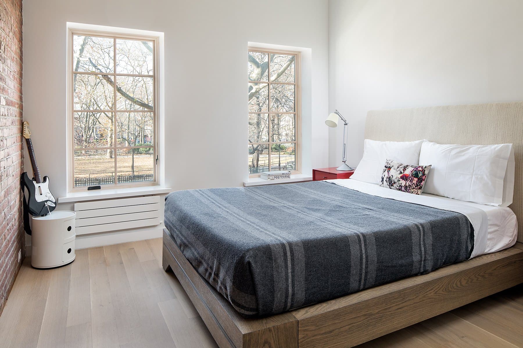 Bedroom with a grey striped blanket, exposed brick and windows onto the street
