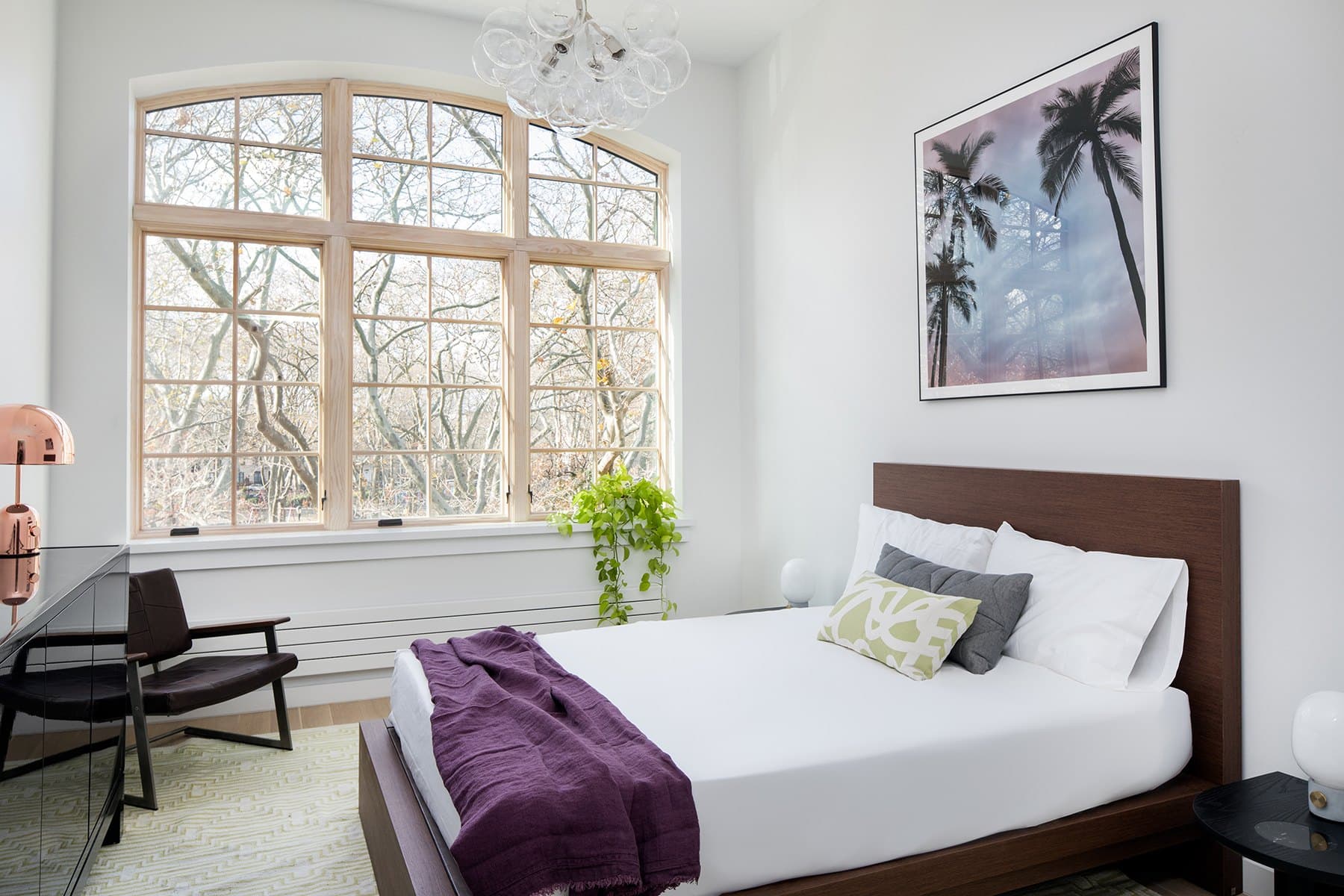Primary bedroom with a walnut bed, white linens and a tall arched window onto bare trees