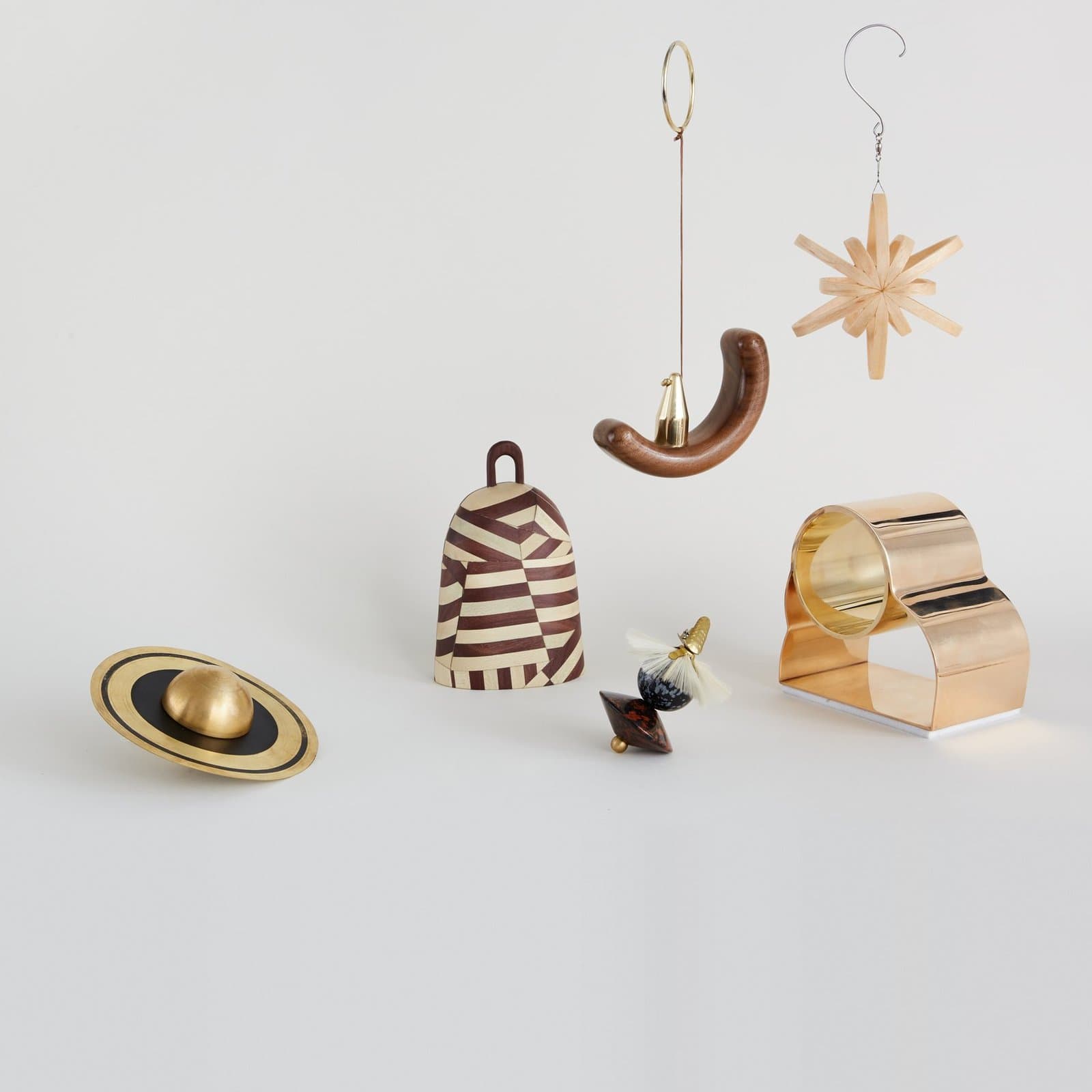 Holiday ornaments by independent designers for WorkOf: a brass Saturn by Richard Clarkson, a striped bell by Crump and Kwash, a walnut crescent by Fernweh Woodworking and a straw star by Harold