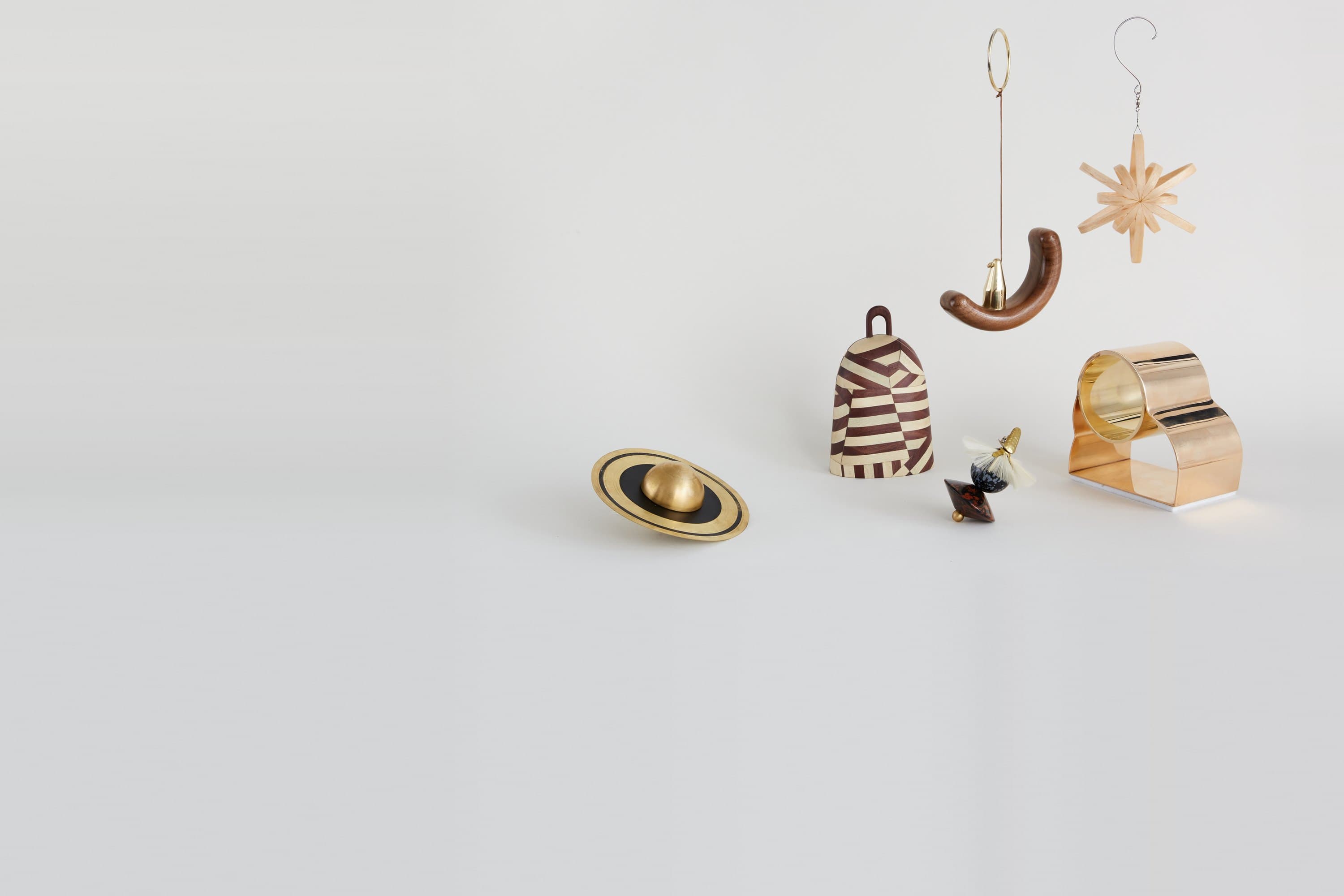 Holiday ornaments by independent designers for WorkOf: a brass Saturn by Richard Clarkson, a striped bell by Crump and Kwash, a walnut crescent by Fernweh Woodworking and a straw star by Harold