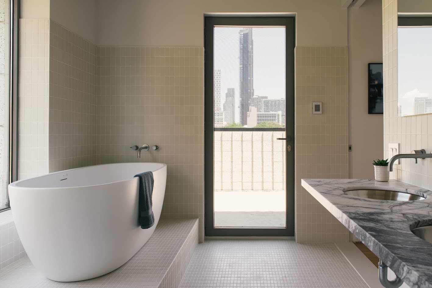 Bathroom with a freestanding tub, white tile, a marble vanity and a glass door to a terrace