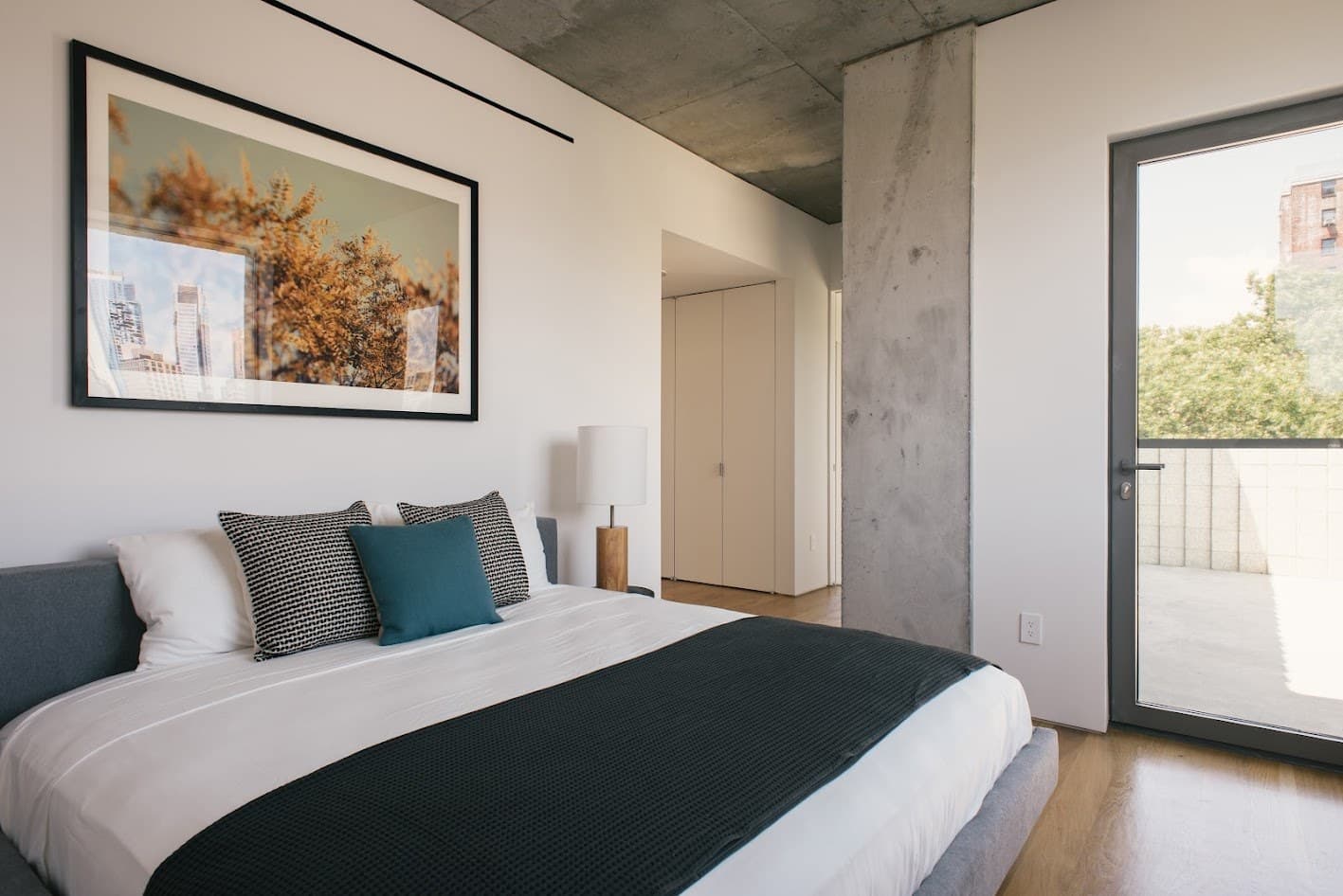 Primary bedroom at 450 Warren with grey and teal pillows, a black throw and an autumn landscape print over the bed