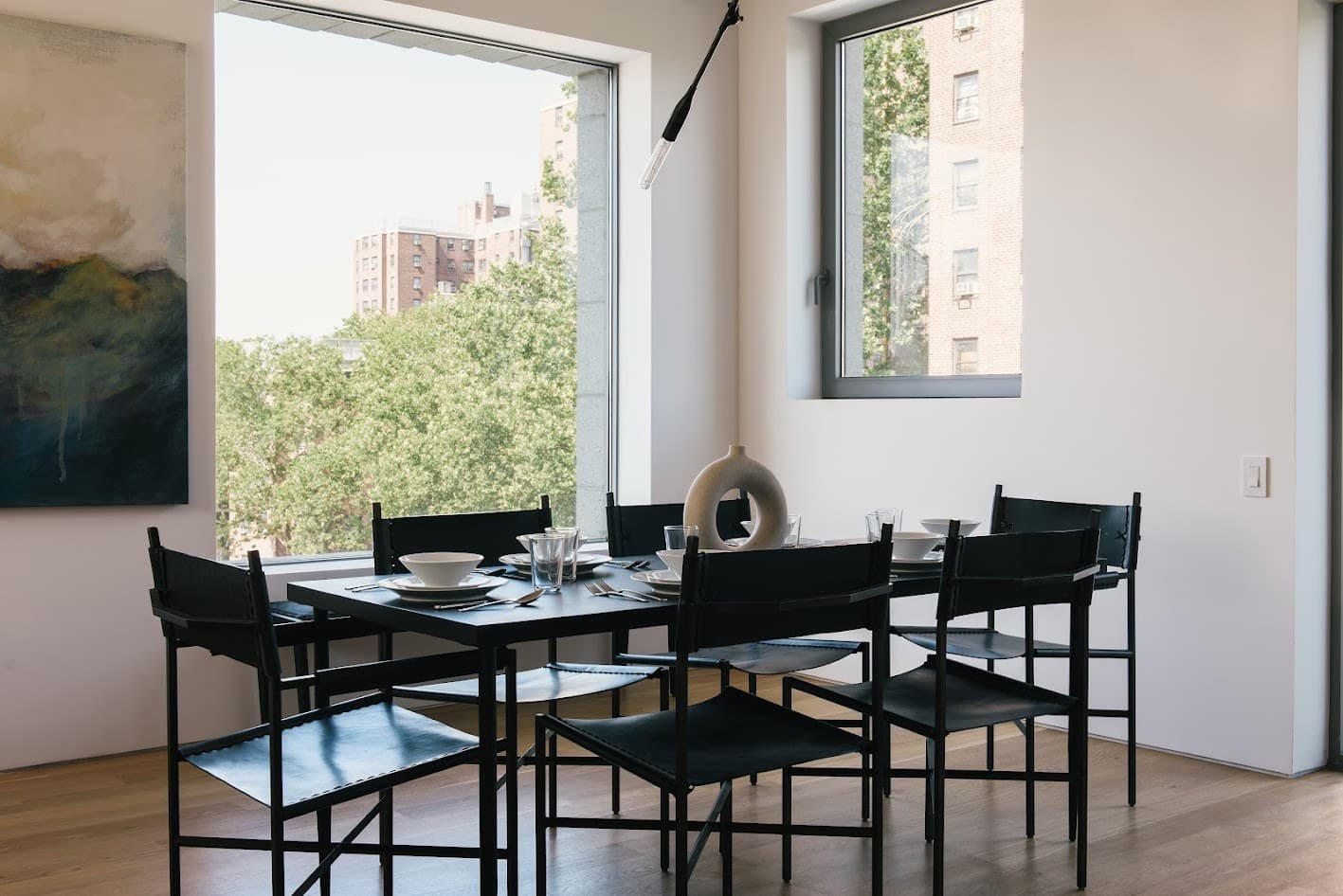 Dining table set with white bowls and a ceramic ring vase, black leather chairs and an oak bench beneath a sculptural pendant at 450 Warren