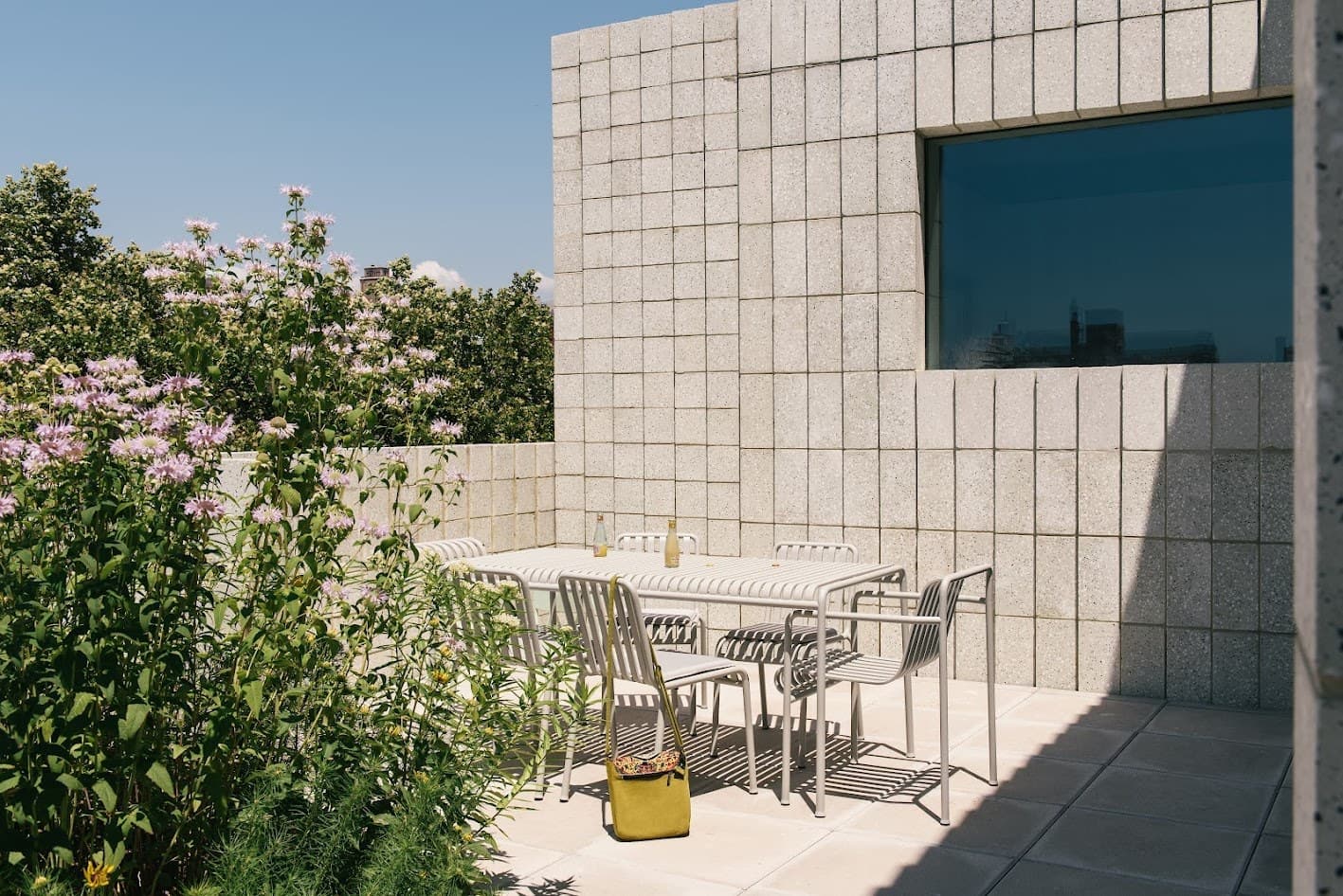 Planted roof terrace at 450 Warren in Gowanus with white metal café tables and chairs against a textured concrete wall