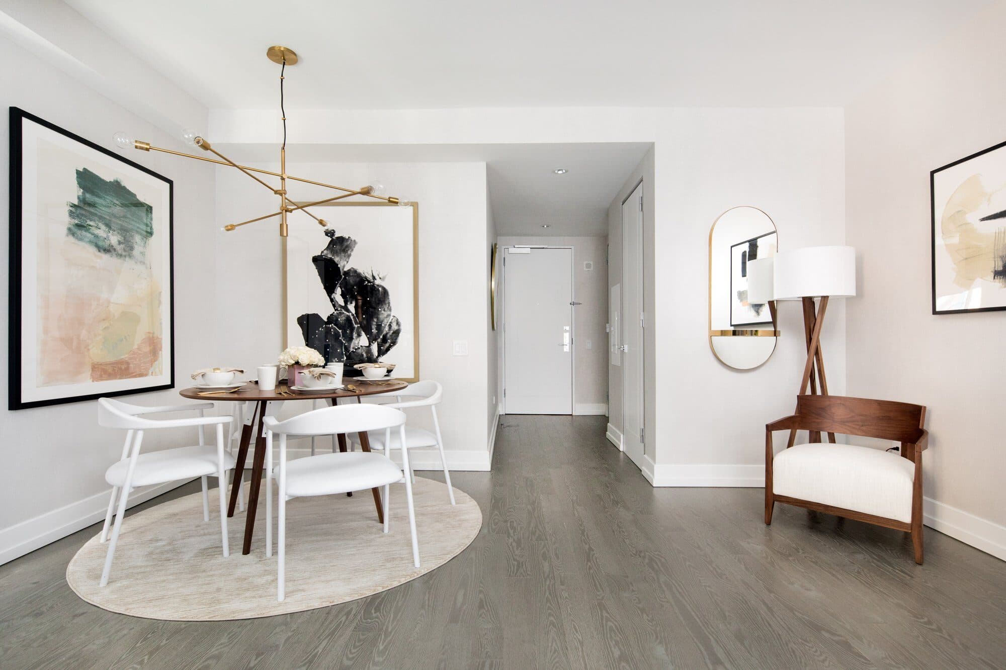 Round dining table with white chairs on a circular rug beneath a brass sputnik pendant