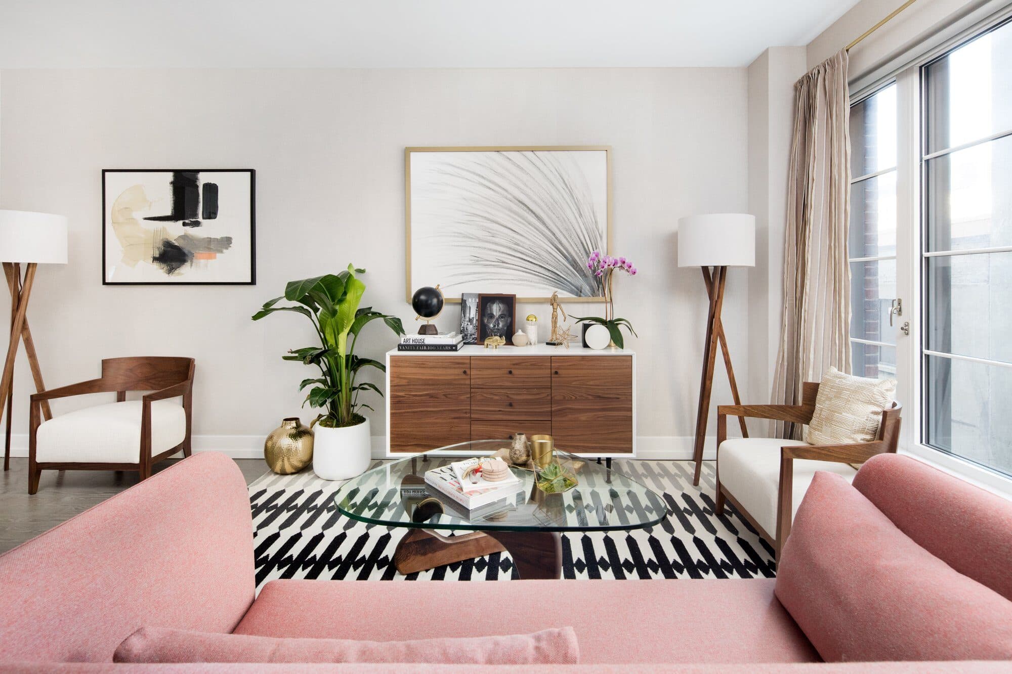 Living room with a blush sofa, a glass coffee table on a striped rug, a walnut credenza and a pair of tripod floor lamps