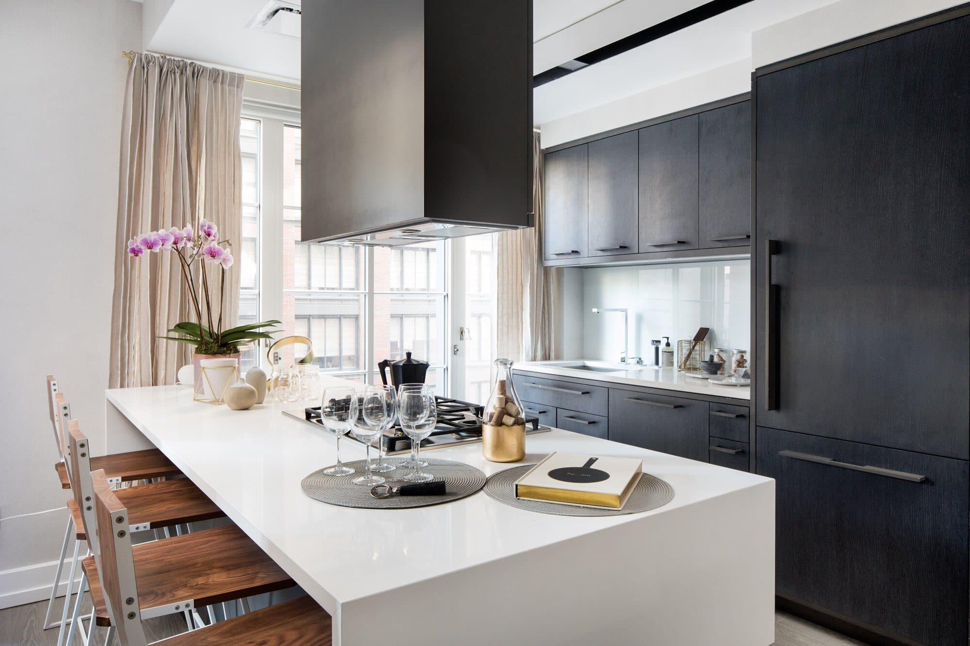Dark oak kitchen with a white waterfall island, walnut counter stools and a black range hood