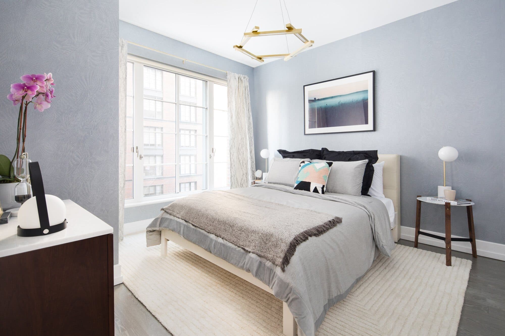Bedroom with powder-blue walls, a brass ceiling fixture and a framed seascape over the bed