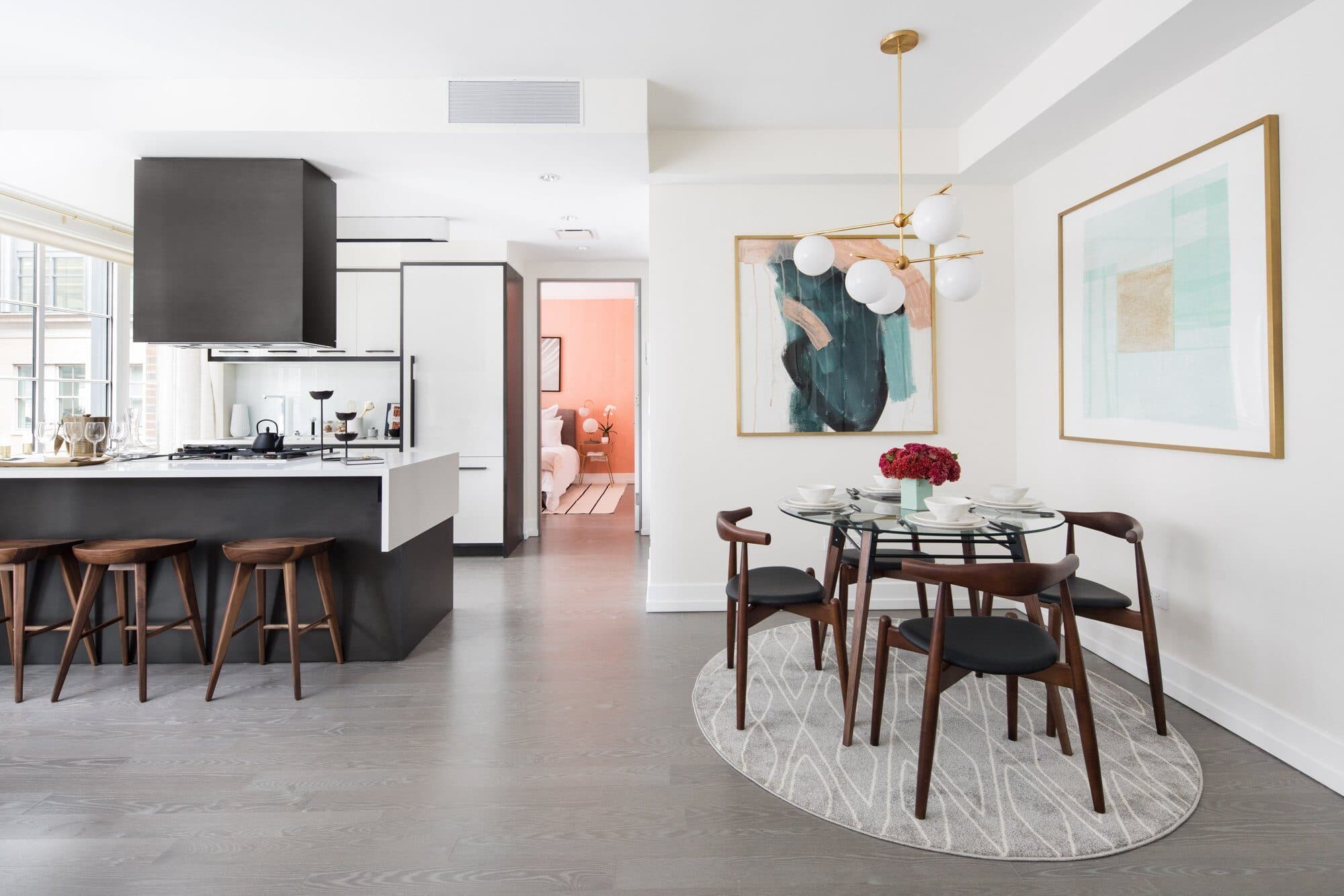 Bright open kitchen and dining area with a white island, walnut stools and a round dining table under a globe pendant