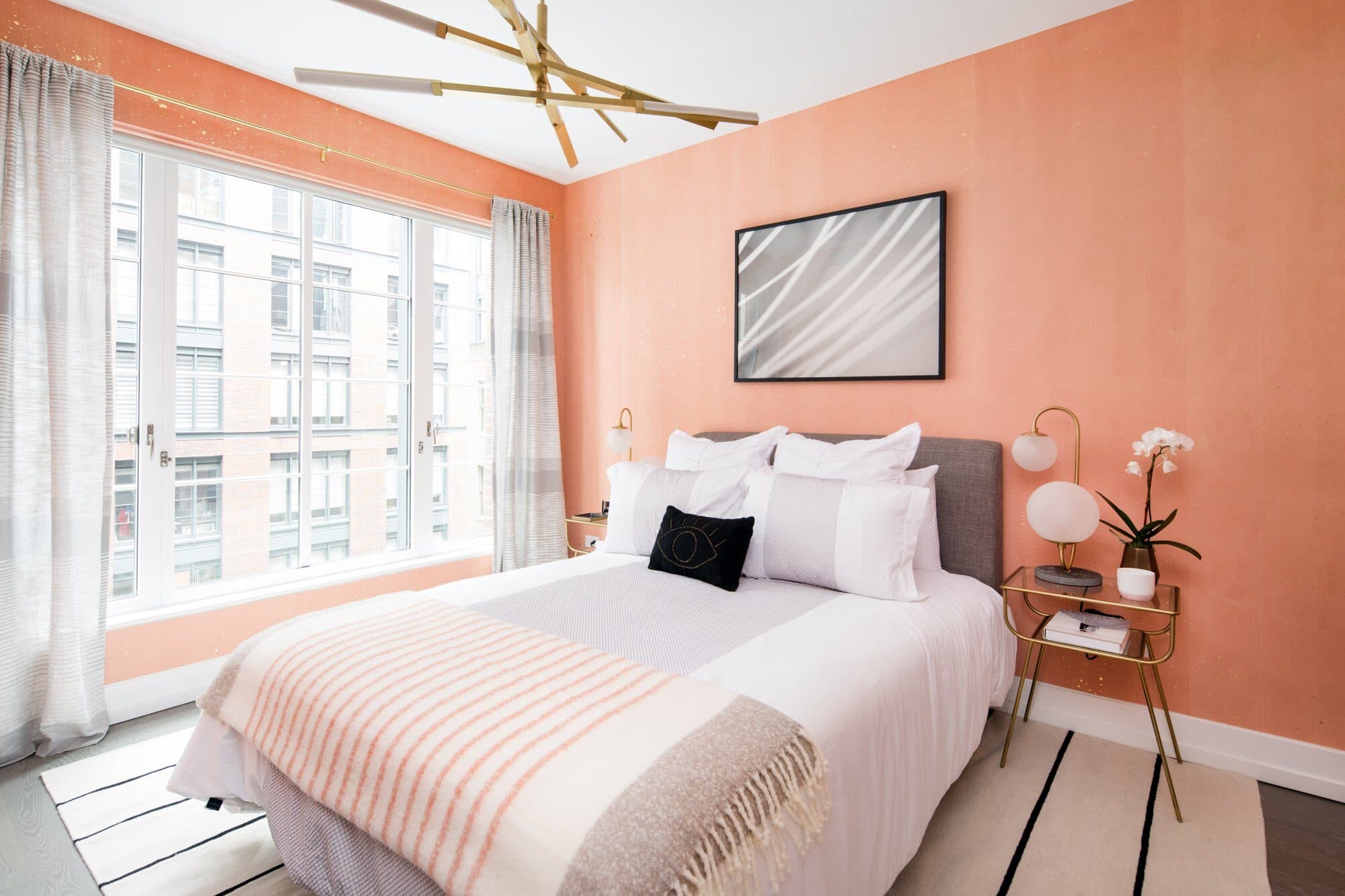 Bedroom with a coral wall, a grey upholstered bed with a striped blush throw and a brass sputnik fixture