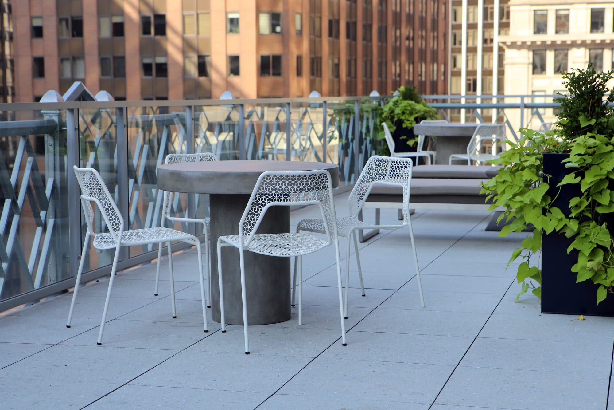 70 Pine rooftop terrace with concrete café tables, white wire chairs and planters among Financial District towers
