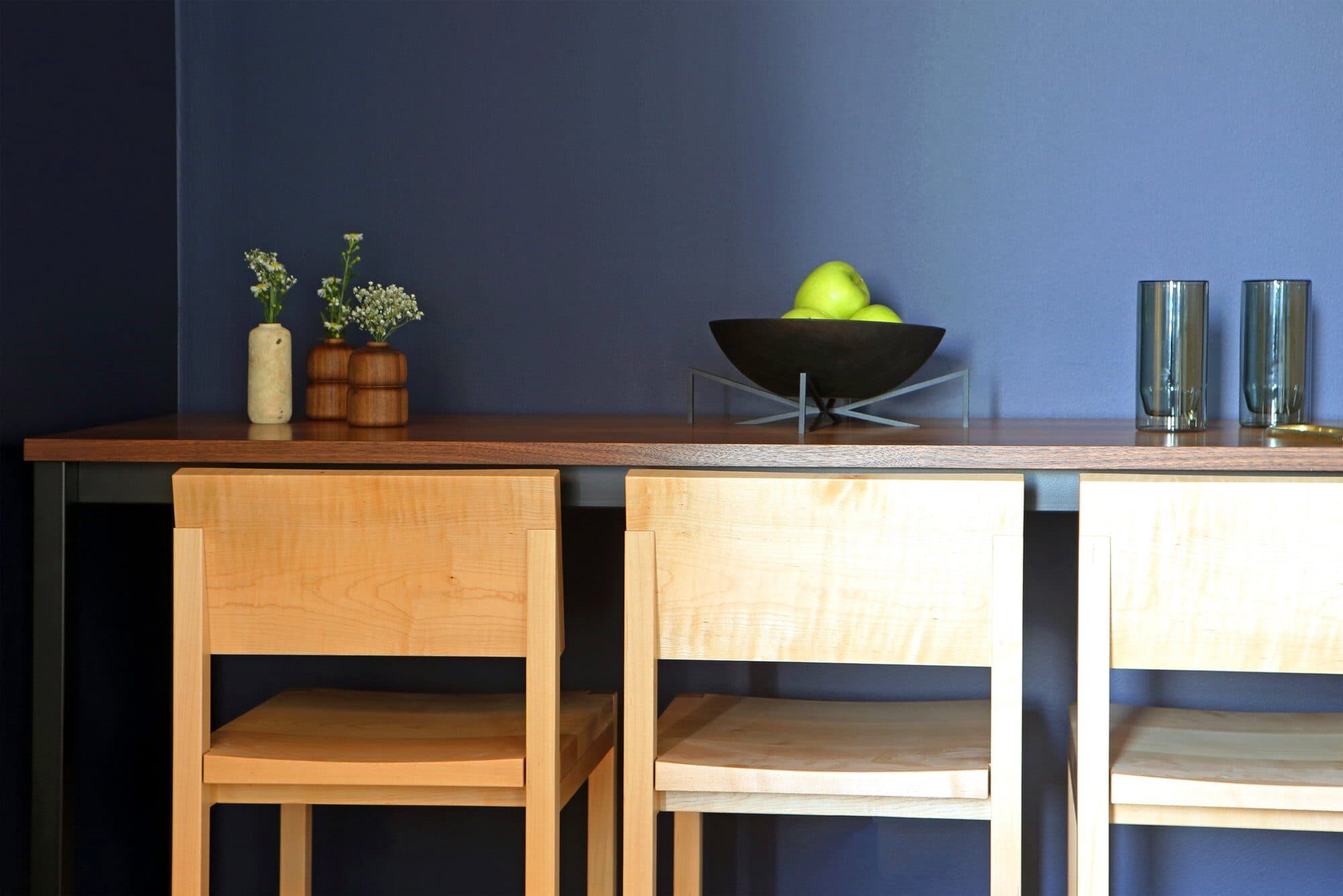 70 Pine resident lounge with a navy wall, a walnut seating counter, maple stools and a bowl of green apples