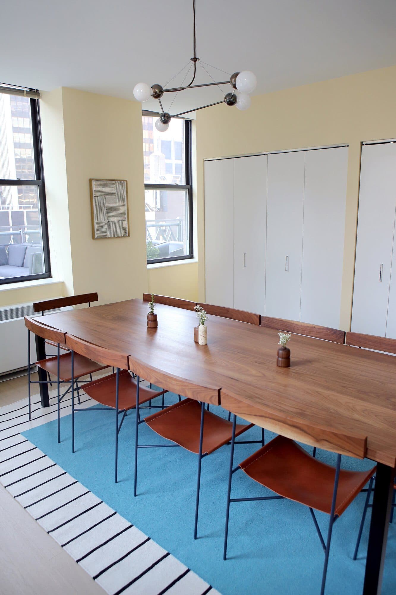 70 Pine conference room with a walnut table and leather sling chairs under a globe chandelier on a blue striped rug