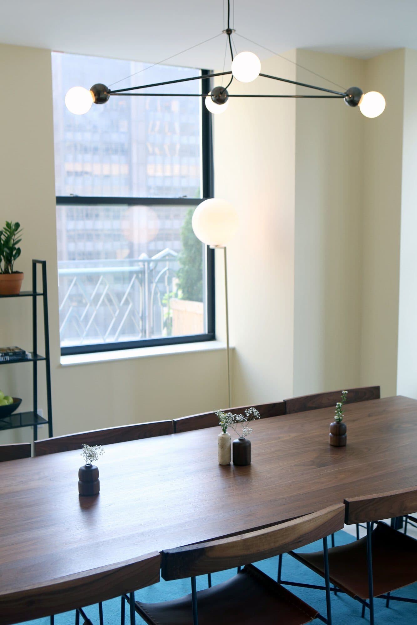 Conference table with small vases by the window and a globe chandelier overhead