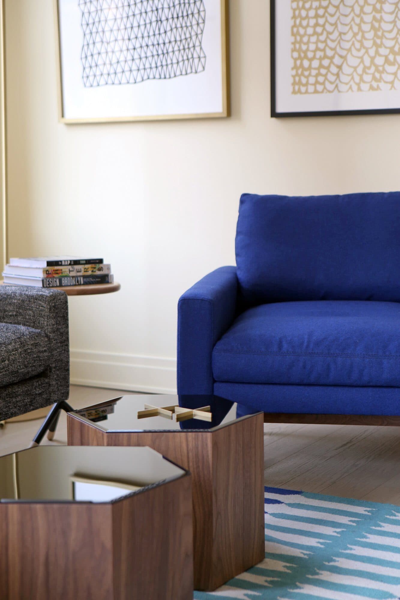 Cobalt armchair beside a walnut hexagonal side table under framed prints