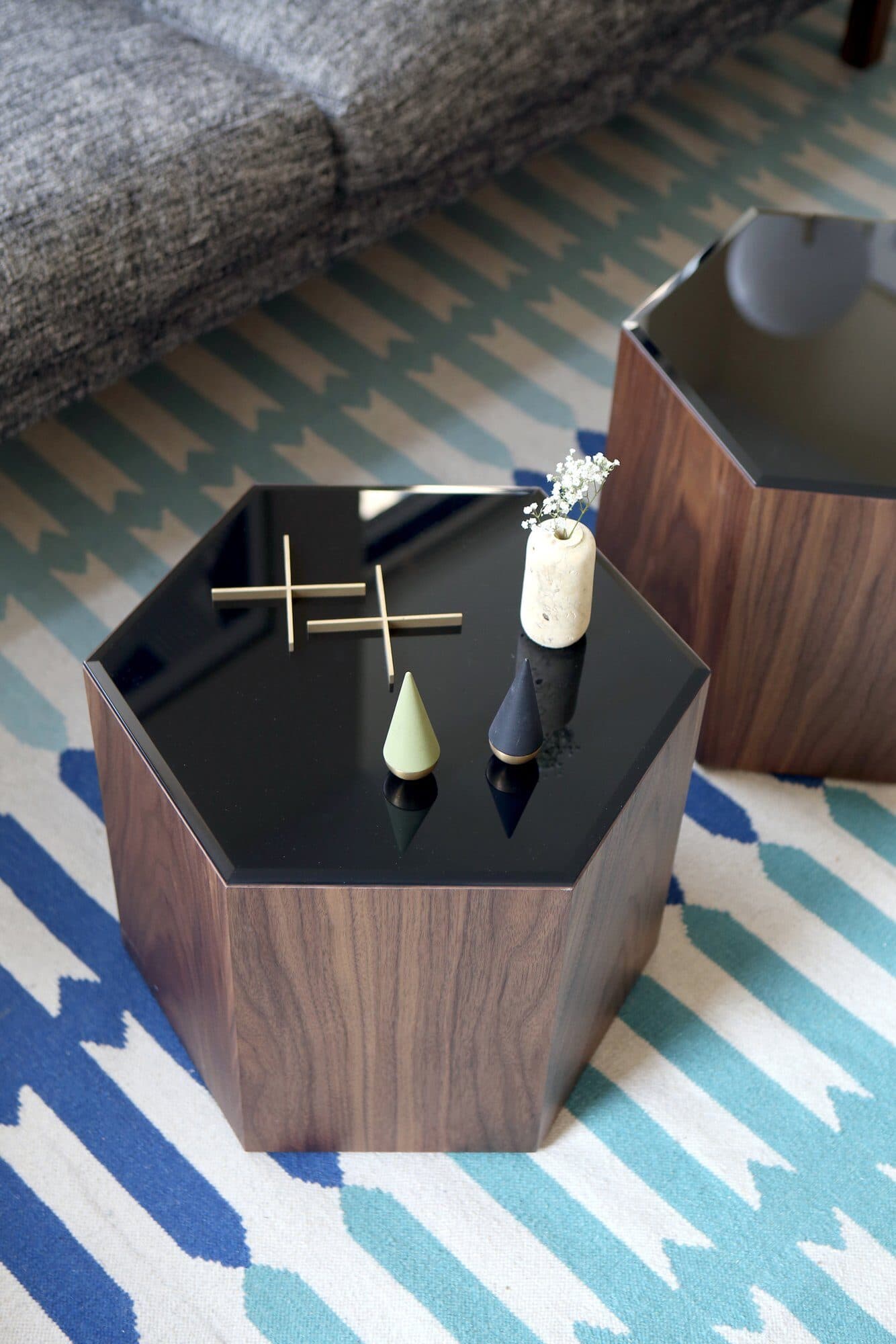 Hexagonal walnut table with a black glass top on a blue rug