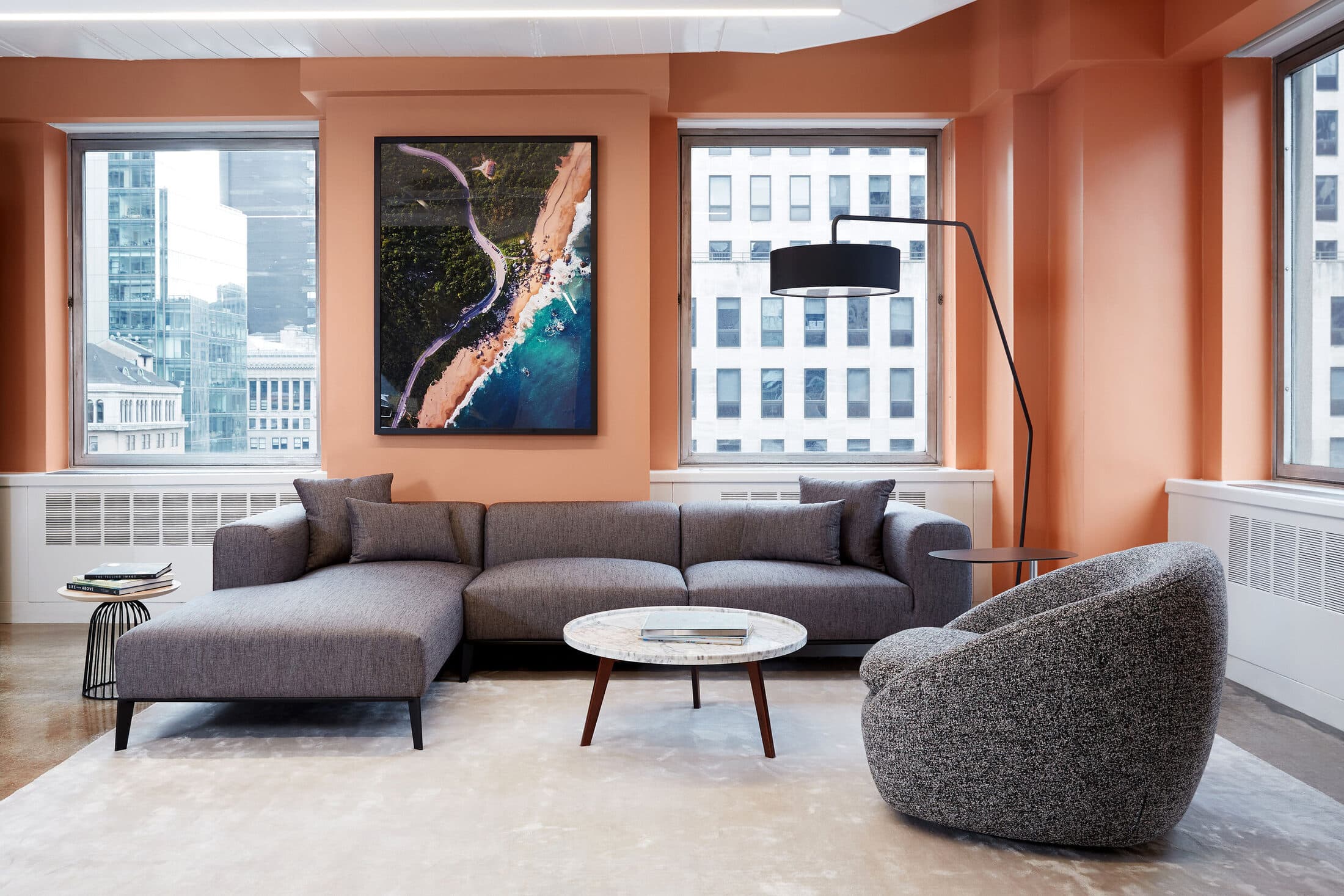 Lounge seating with a grey sectional, a swivel chair, and a round marble table beneath an aerial photograph