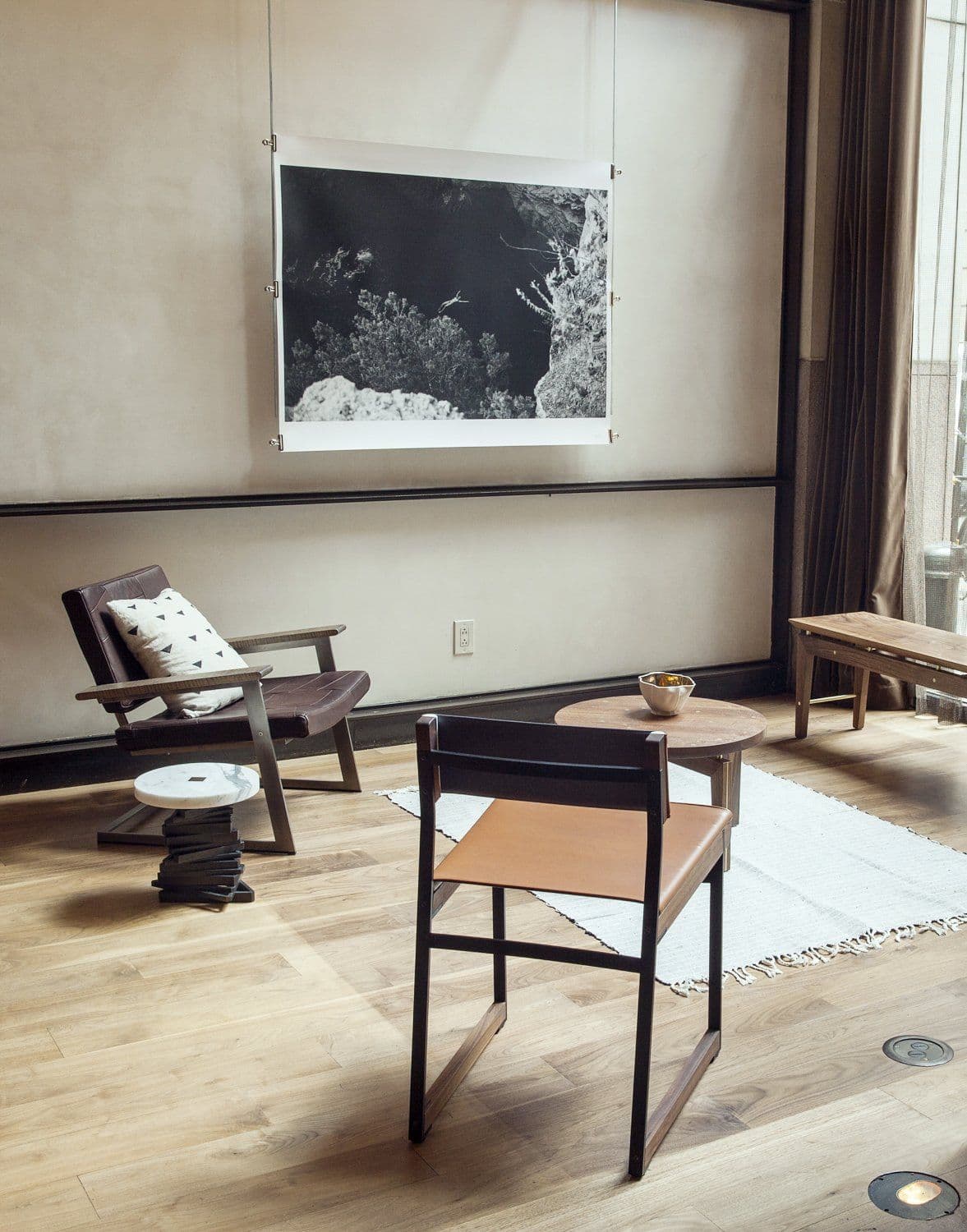 Brown leather lounge chair and a black steel chair with a tan leather sling seat beneath a photograph of a rocky coastline