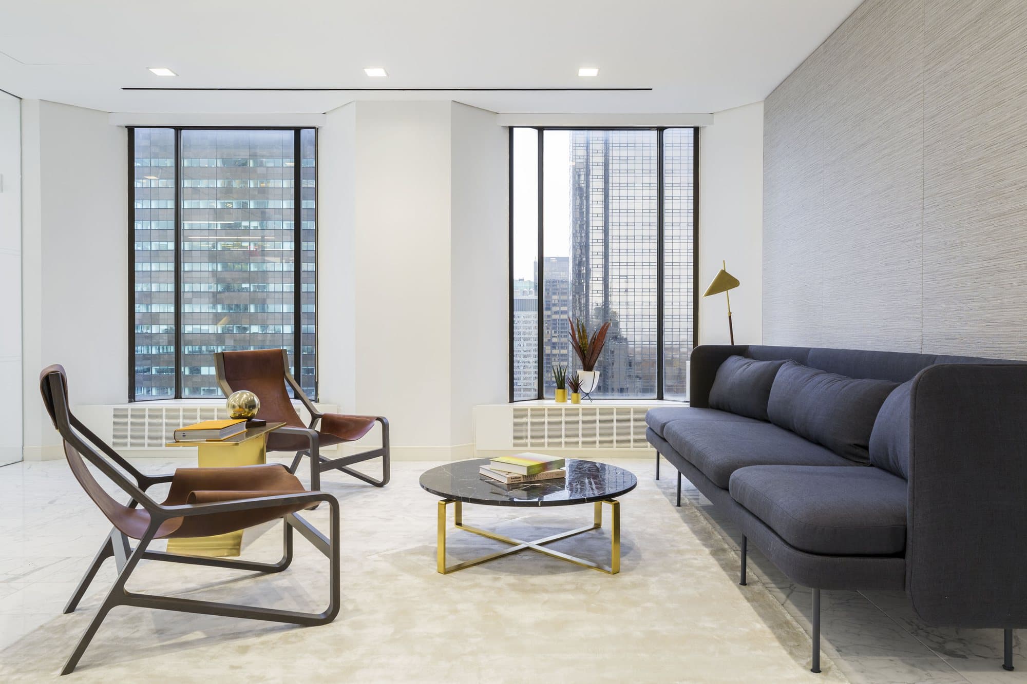 Corner lounge with cognac leather armchairs, a charcoal sofa and a marble coffee table before floor-to-ceiling windows