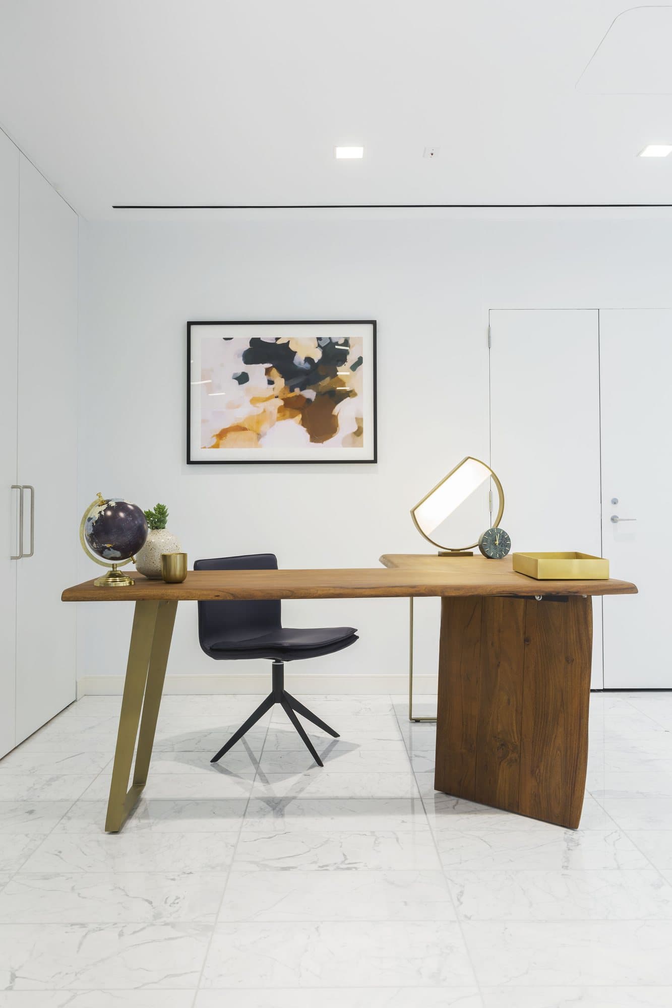 Reception desk in walnut and brass with a black swivel chair beneath an abstract painting