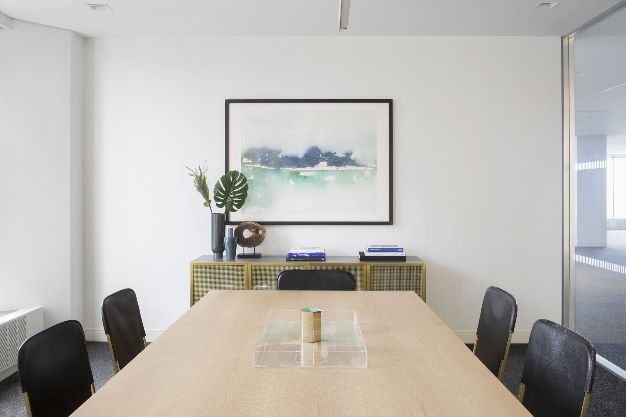Conference room with a pale oak table, black chairs and a brass credenza
