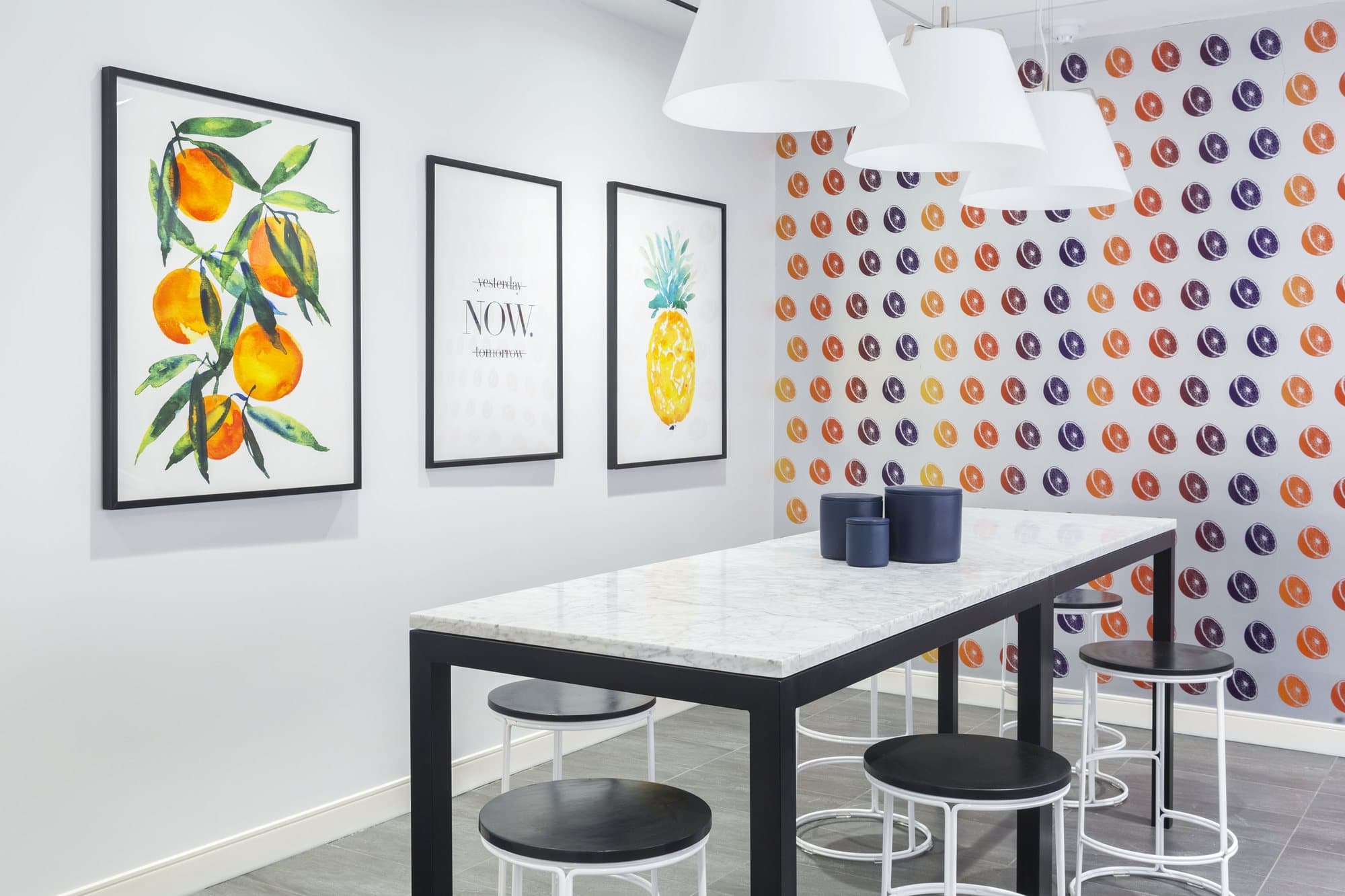 Marble communal table with black and white stools beneath white pendants and botanical prints