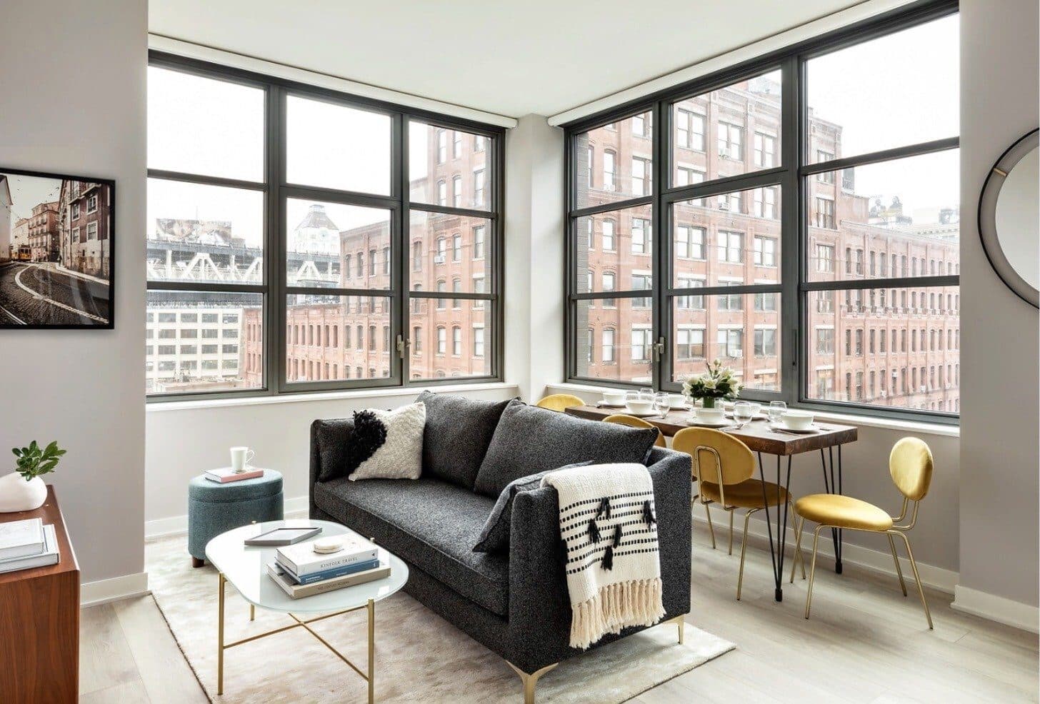 Corner living room at Magnolia with a charcoal sofa, gold dining chairs and steel windows overlooking brick buildings