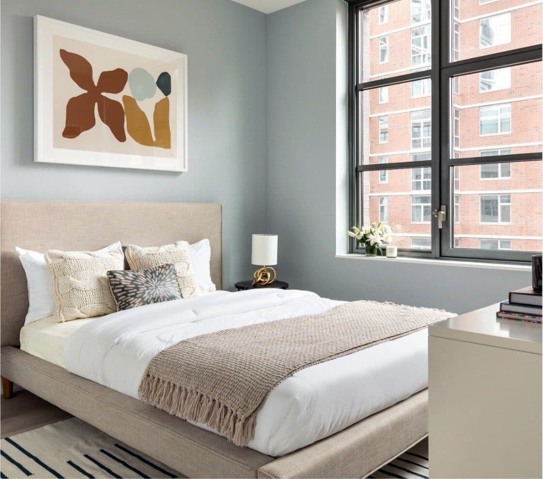 Magnolia model bedroom with blue-grey walls, a cream upholstered bed and a large abstract print in rust and gold