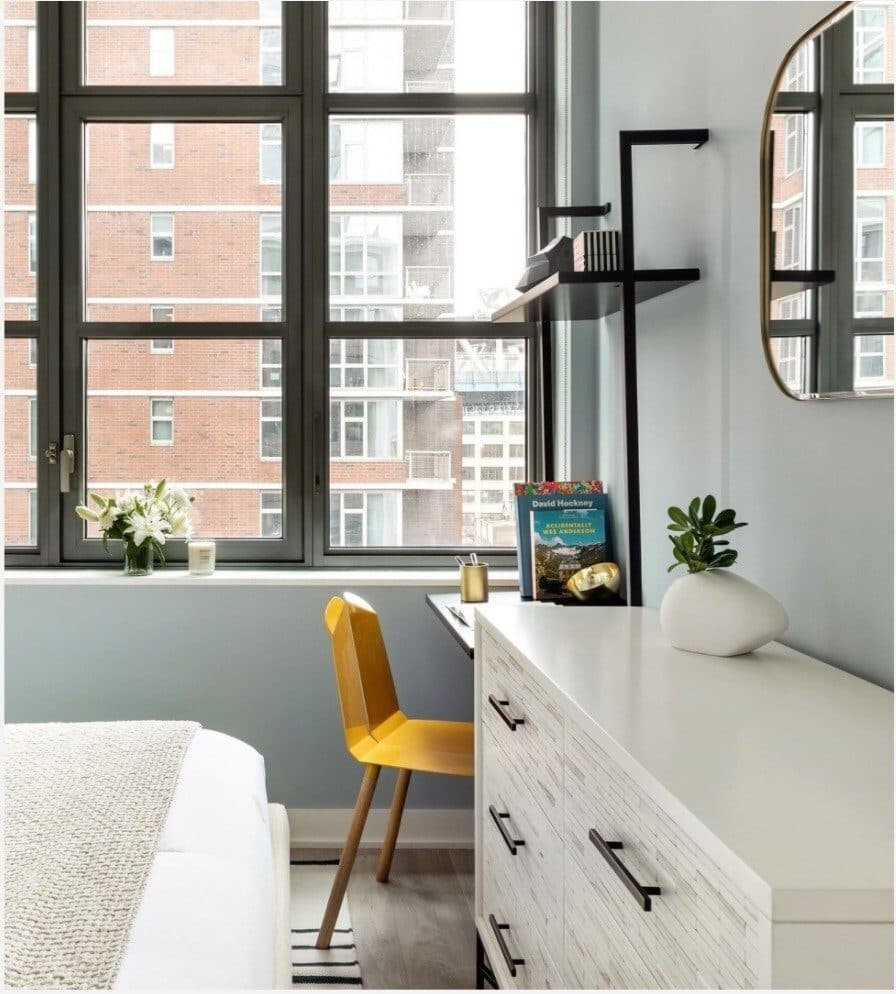 Home office corner with a white desk, a yellow chair and a round mirror by the window