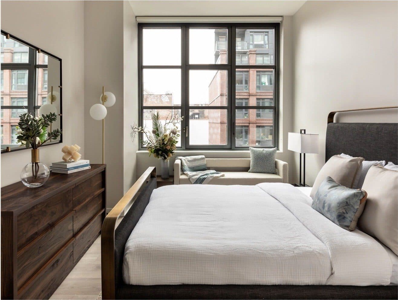Bedroom with a walnut dresser, upholstered bed and a lamp-lit corner window