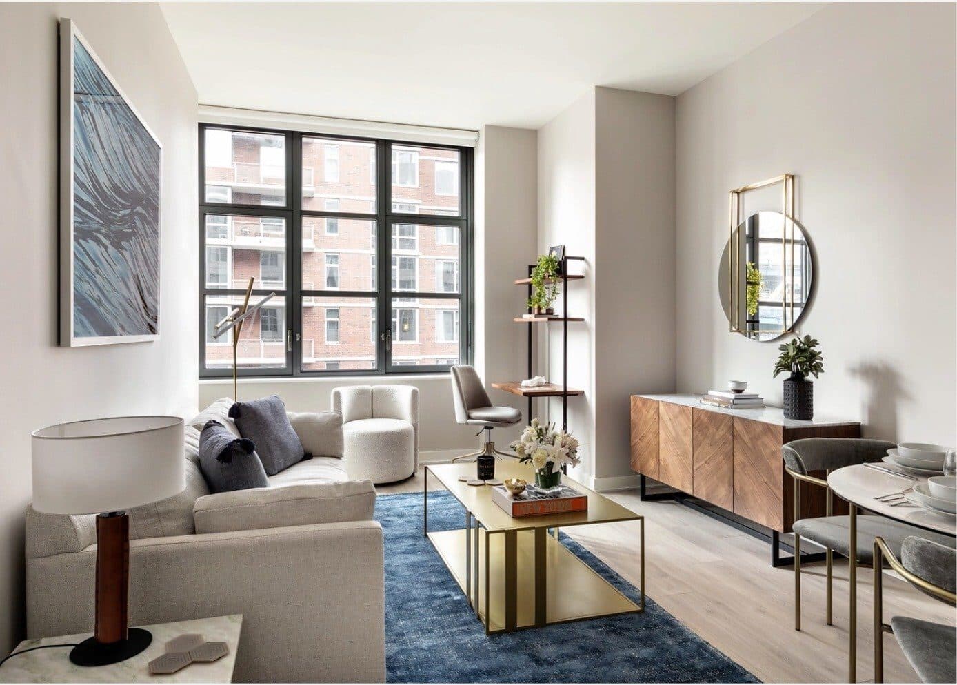 Magnolia one-bedroom living room with a cream sofa, a brass coffee table on a navy rug and a walnut credenza