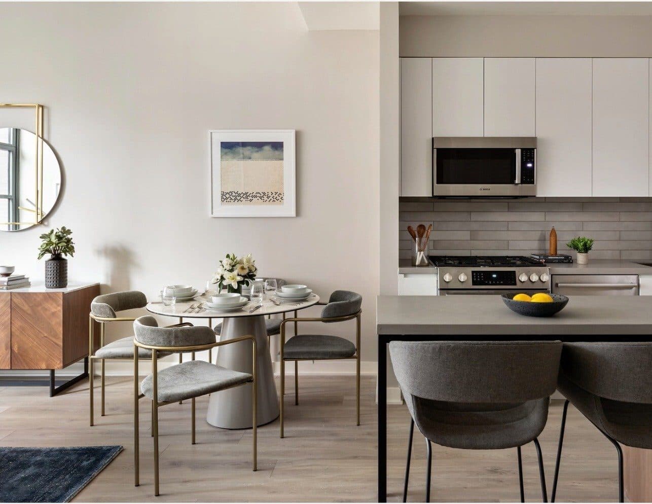 Magnolia model residence dining area with a round table and woven chairs beside a white kitchen, with an abstract beach print on the wall