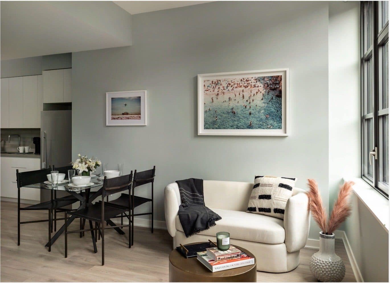 Magnolia studio apartment with a cream lounge chair, a glass dining table with black chairs and a pink-toned art print