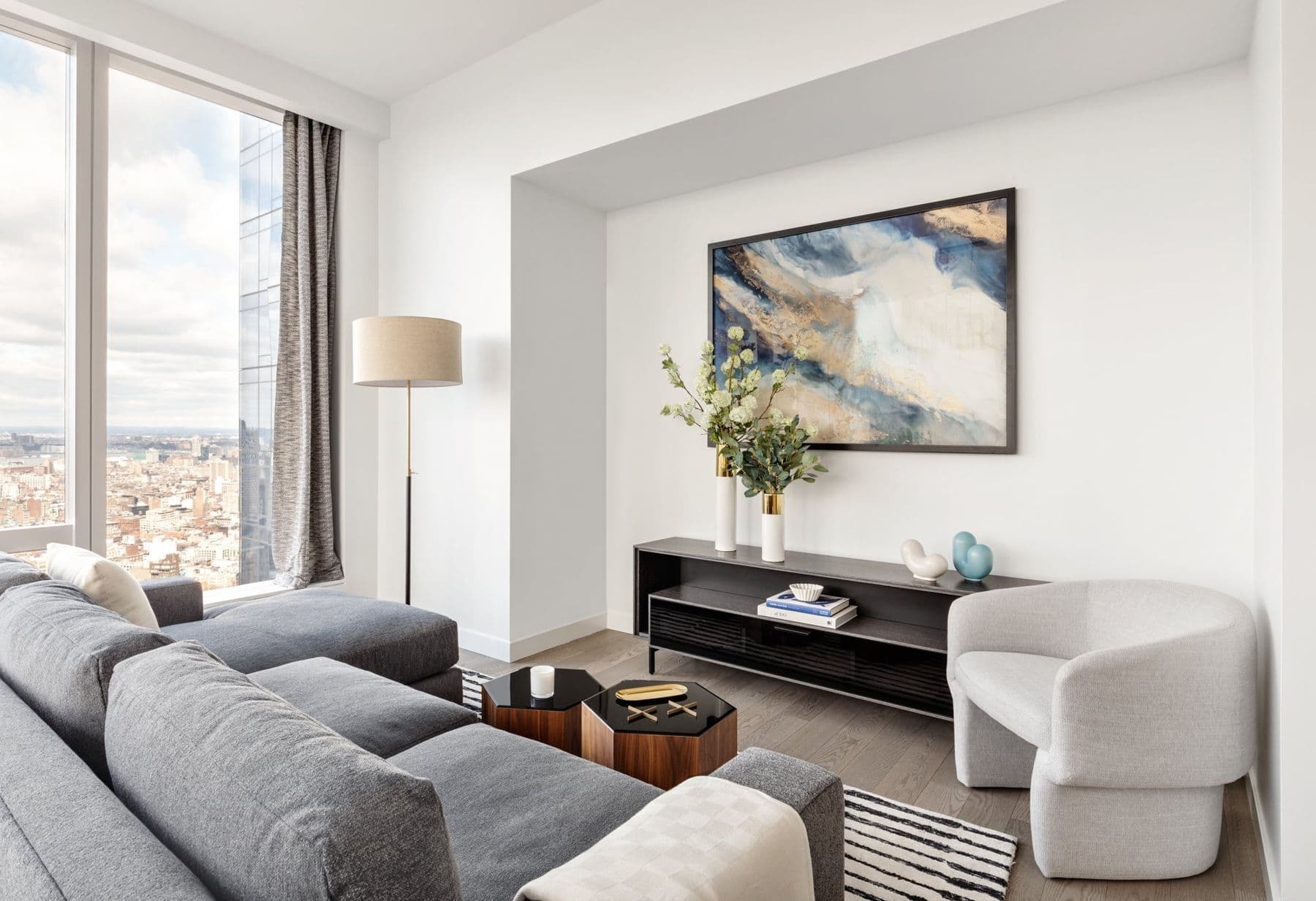 Light living room with a grey sectional, a white lounge chair, and a cloud painting over a low credenza