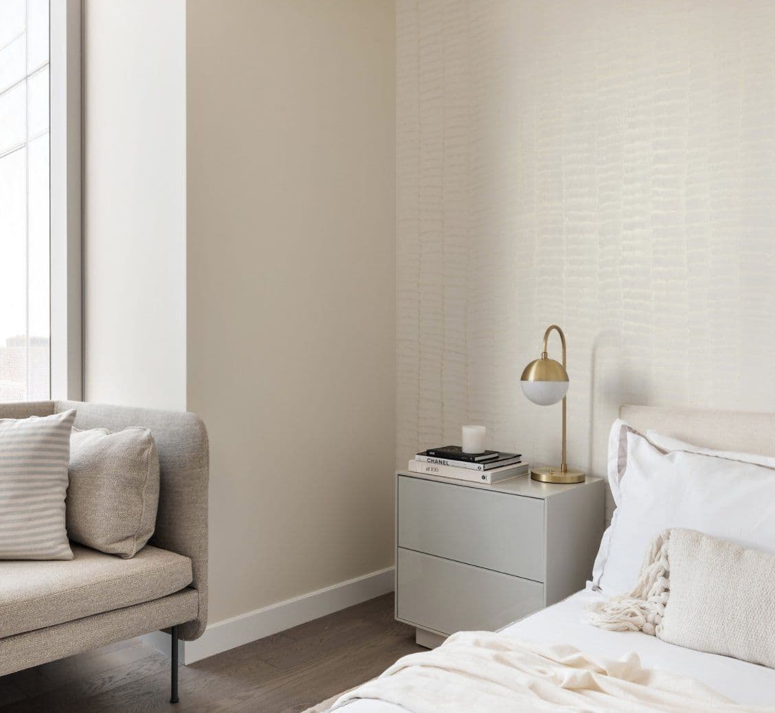 Bedroom corner with a pale textured Sarkos wallcovering behind a brass lamp