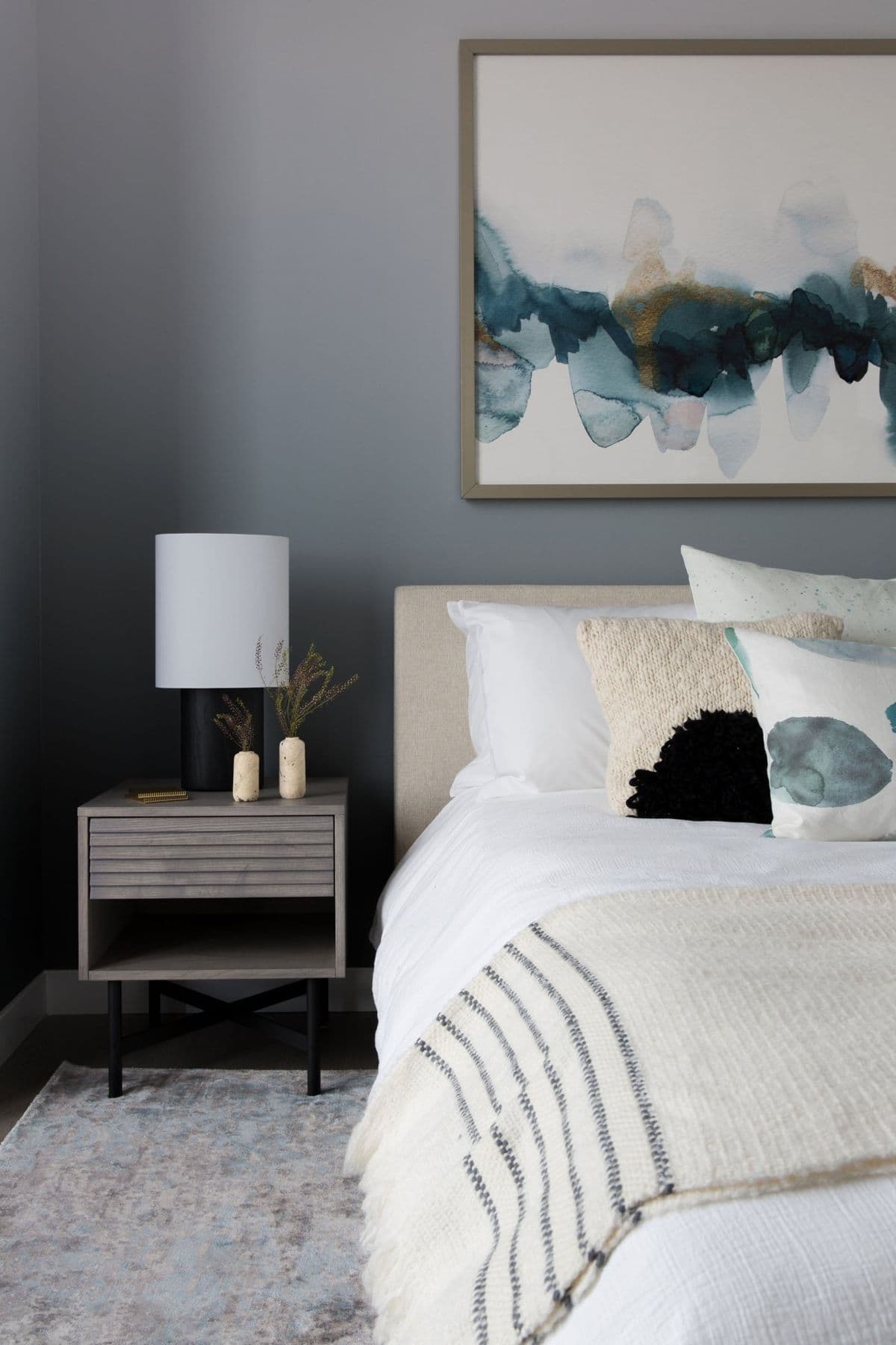 Bedroom with a grey wall, an abstract painting, and layered bedding