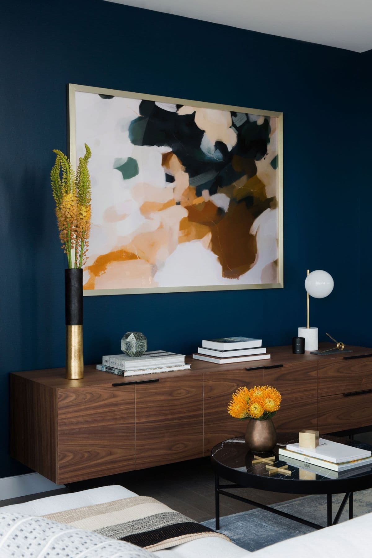 Living room with ink-blue walls, a walnut credenza, and an abstract painting in ochre and navy
