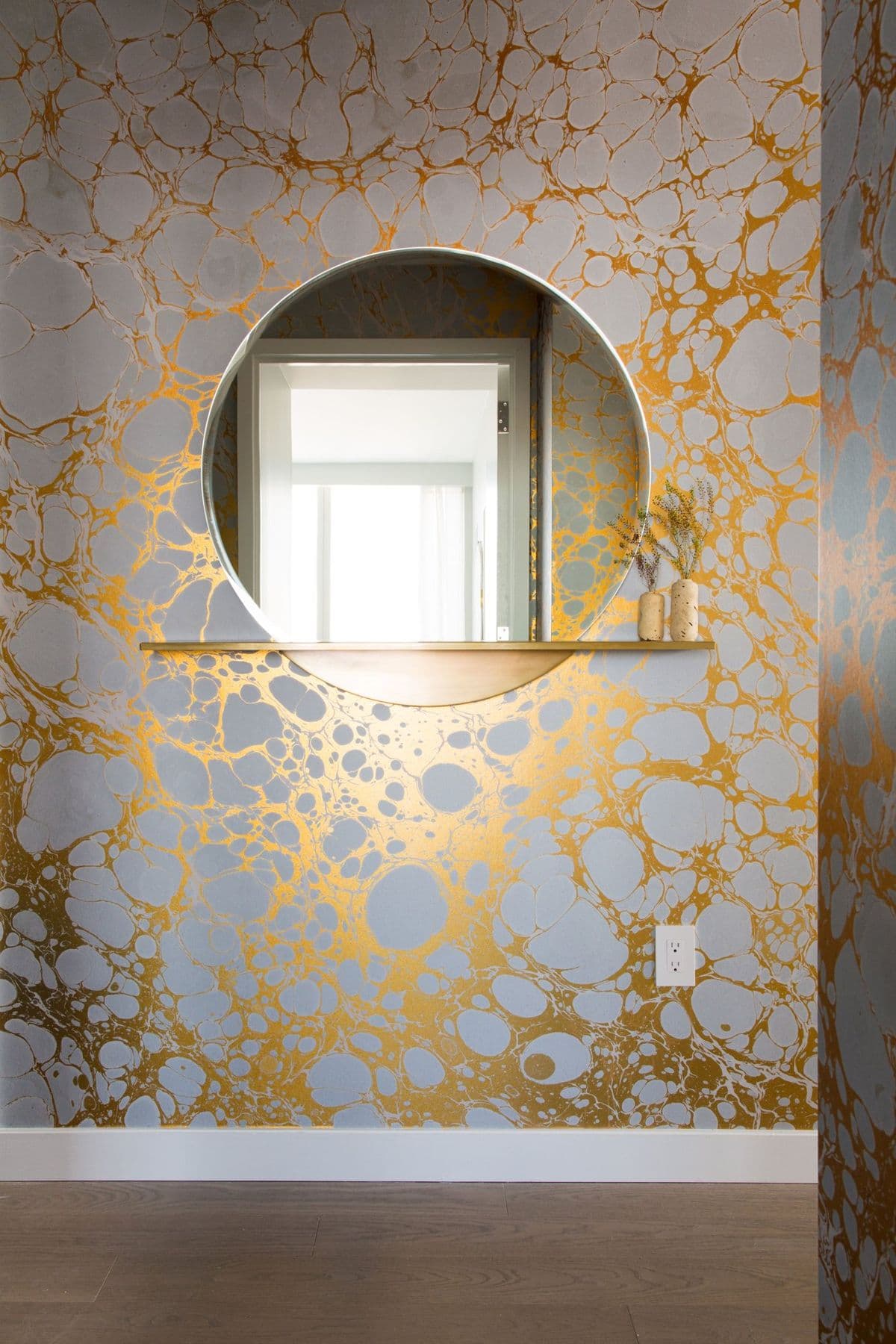 Entry wall in gold marbled wallpaper with a round mirror and a slim shelf