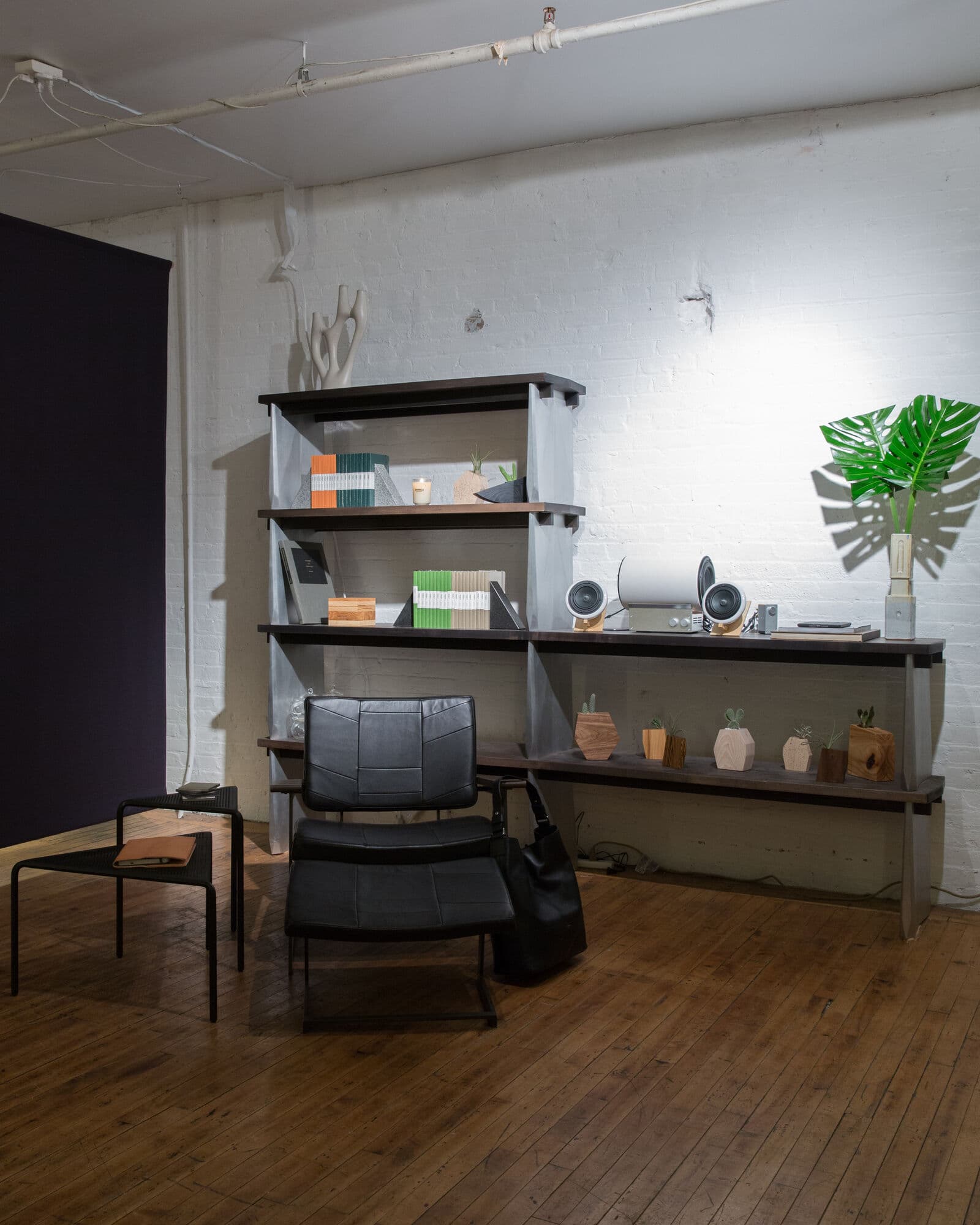 Steel shelving styled with ceramics and Shinola journals beside a black leather lounge chair