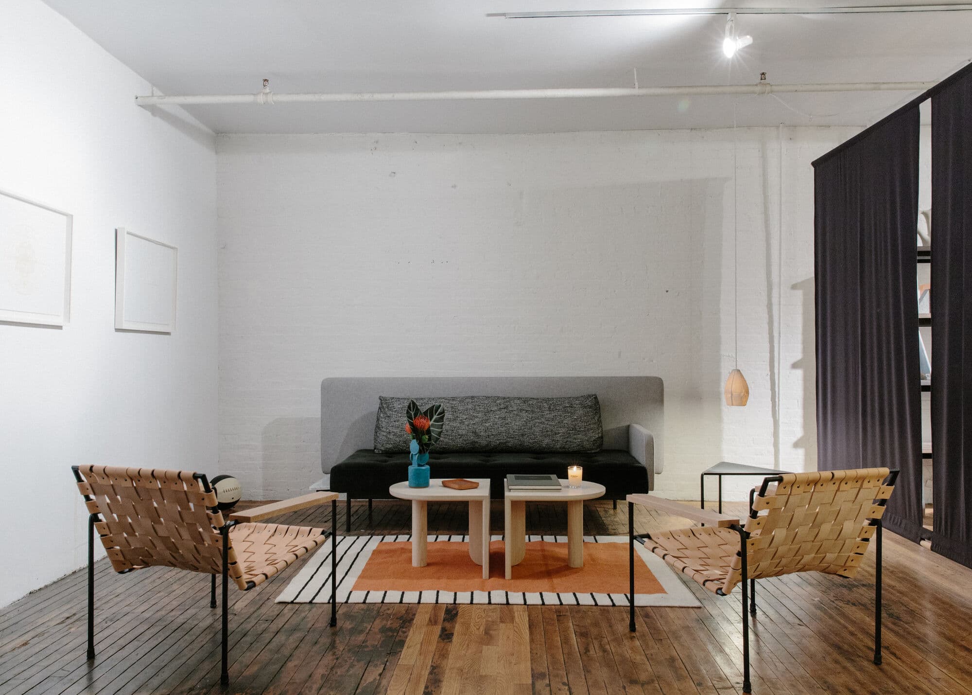 Sitting area with leather sling chairs, a grey sofa and a low table on an orange-striped rug