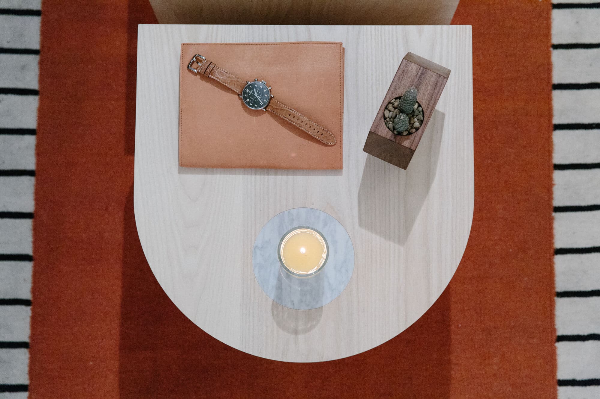 Overhead view of a Shinola watch on a leather tray beside a candle on a white half-round side table